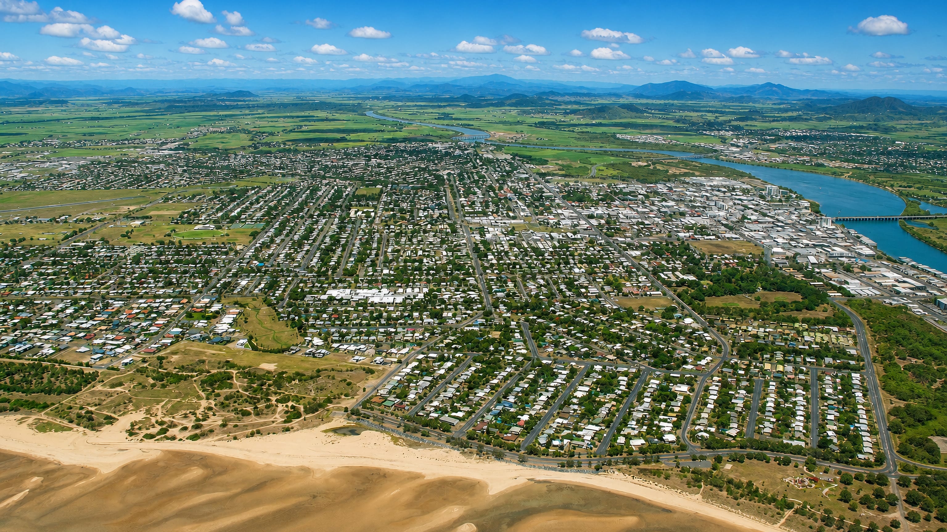 Aerial view of Mackay, Queensland, with its beach, the Pioneer River winding past town and ranges behind.