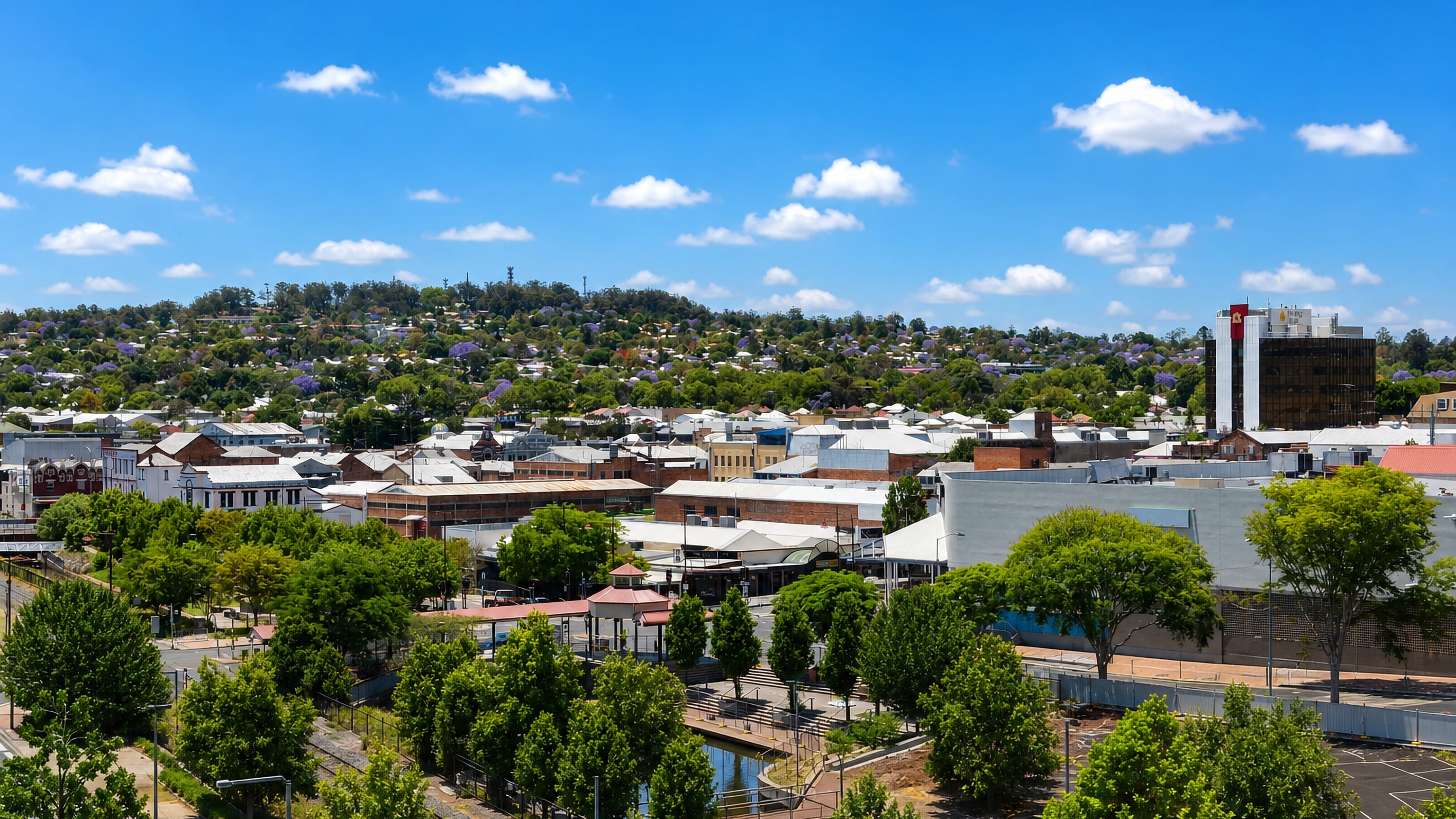 Toowoomba's tin-roofed town centre framed by flowering jacarandas and the wooded range rising behind.
