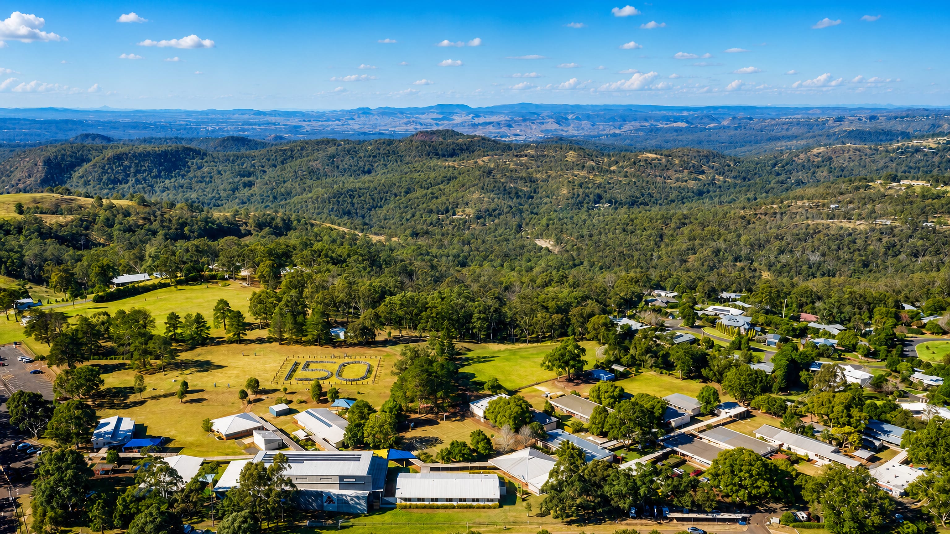 Aerial view of Highfields near Toowoomba, its school grounds and homes spread below the wooded ranges.