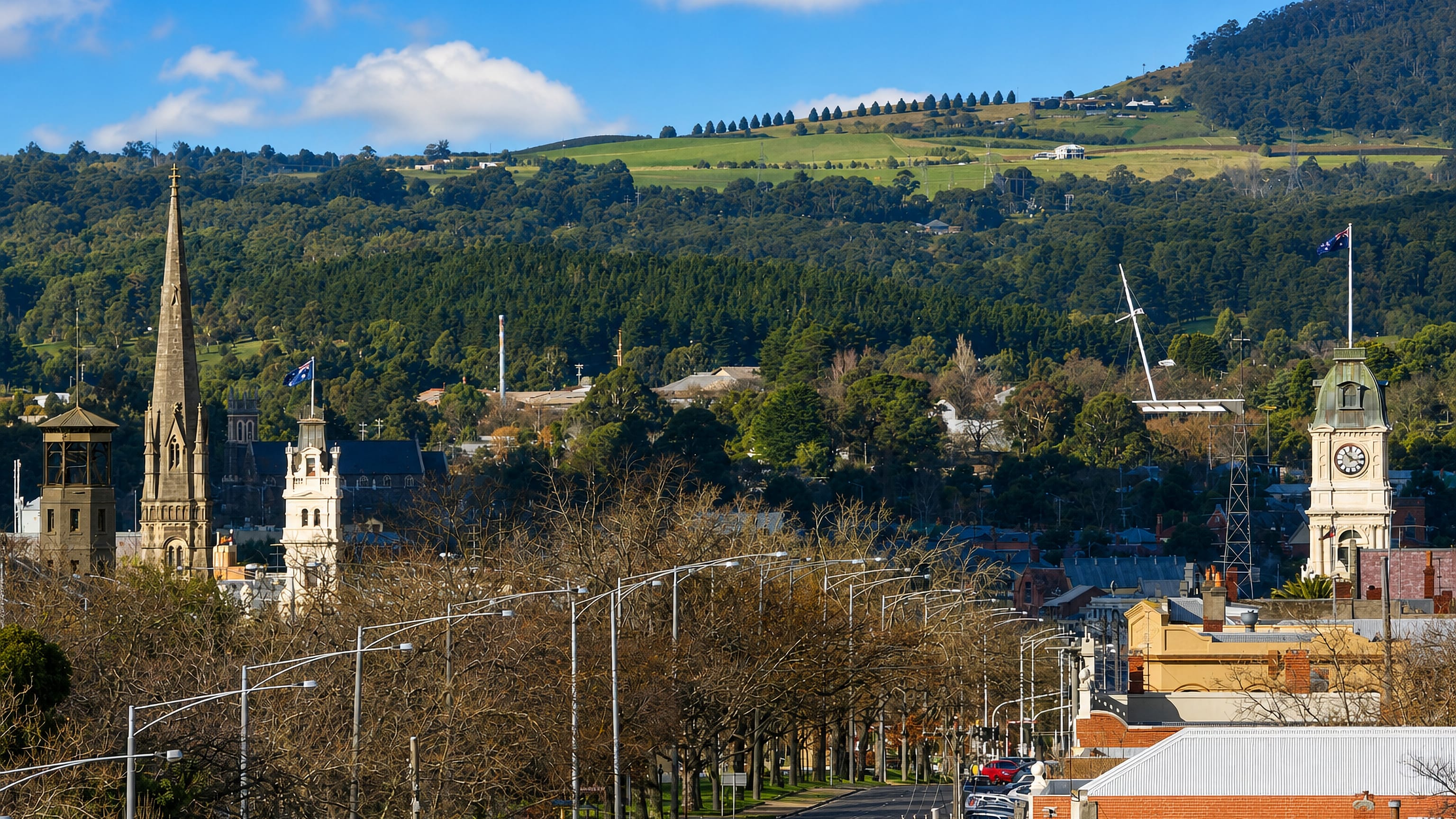 Church spire, town hall clock tower and a tree-lined boulevard below green hills in Ballarat Central.