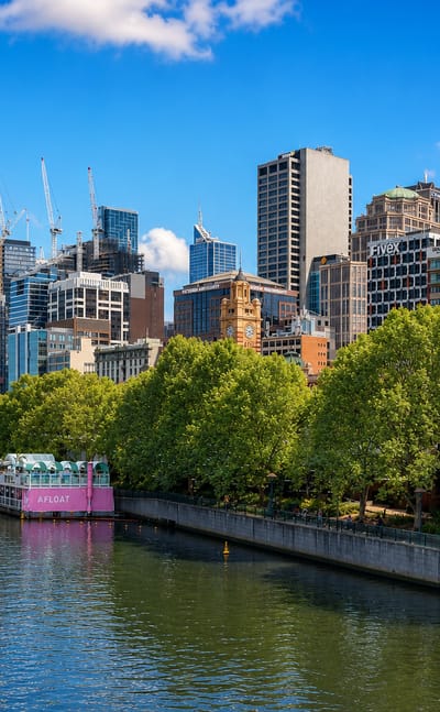 Melbourne city centre skyline along the Yarra River, with the Southbank promenade, plane trees and a pedestrian bridge
