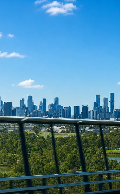 Melbourne CBD skyline on the horizon viewed across parkland from an elevated road in West Melbourne.