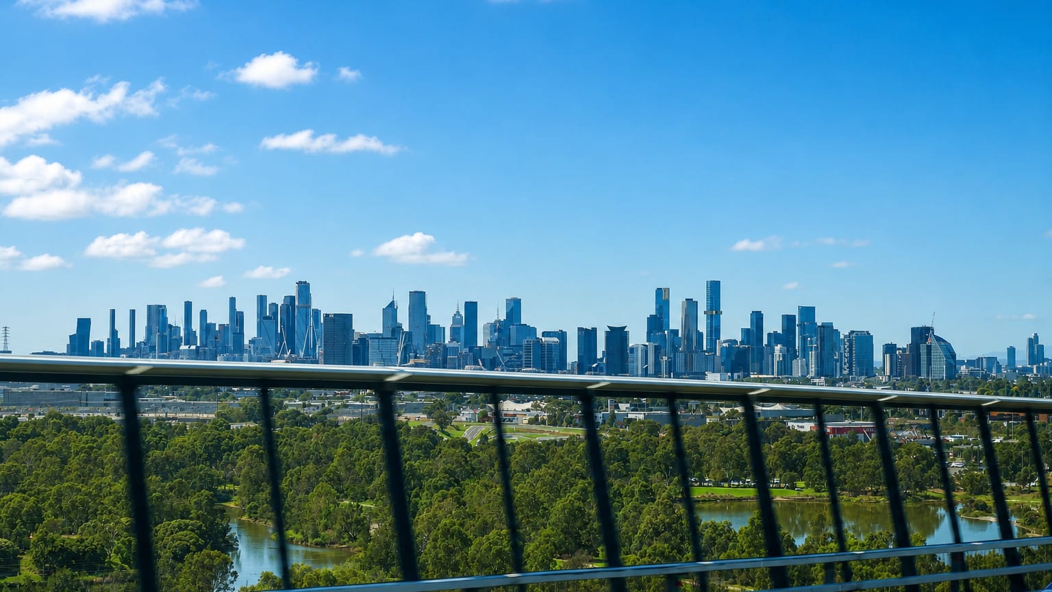 Melbourne CBD skyline on the horizon viewed across parkland from an elevated road in West Melbourne.