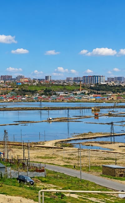 Oil-field flats with pumping derricks fronting a low-rise town and distant Baku skyline at Ramana on the Absheron peninsula
