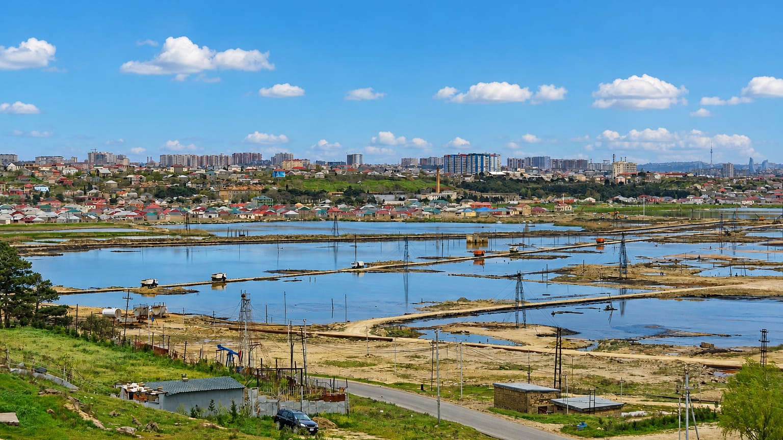 Oil-field flats with pumping derricks fronting a low-rise town and distant Baku skyline at Ramana on the Absheron peninsula