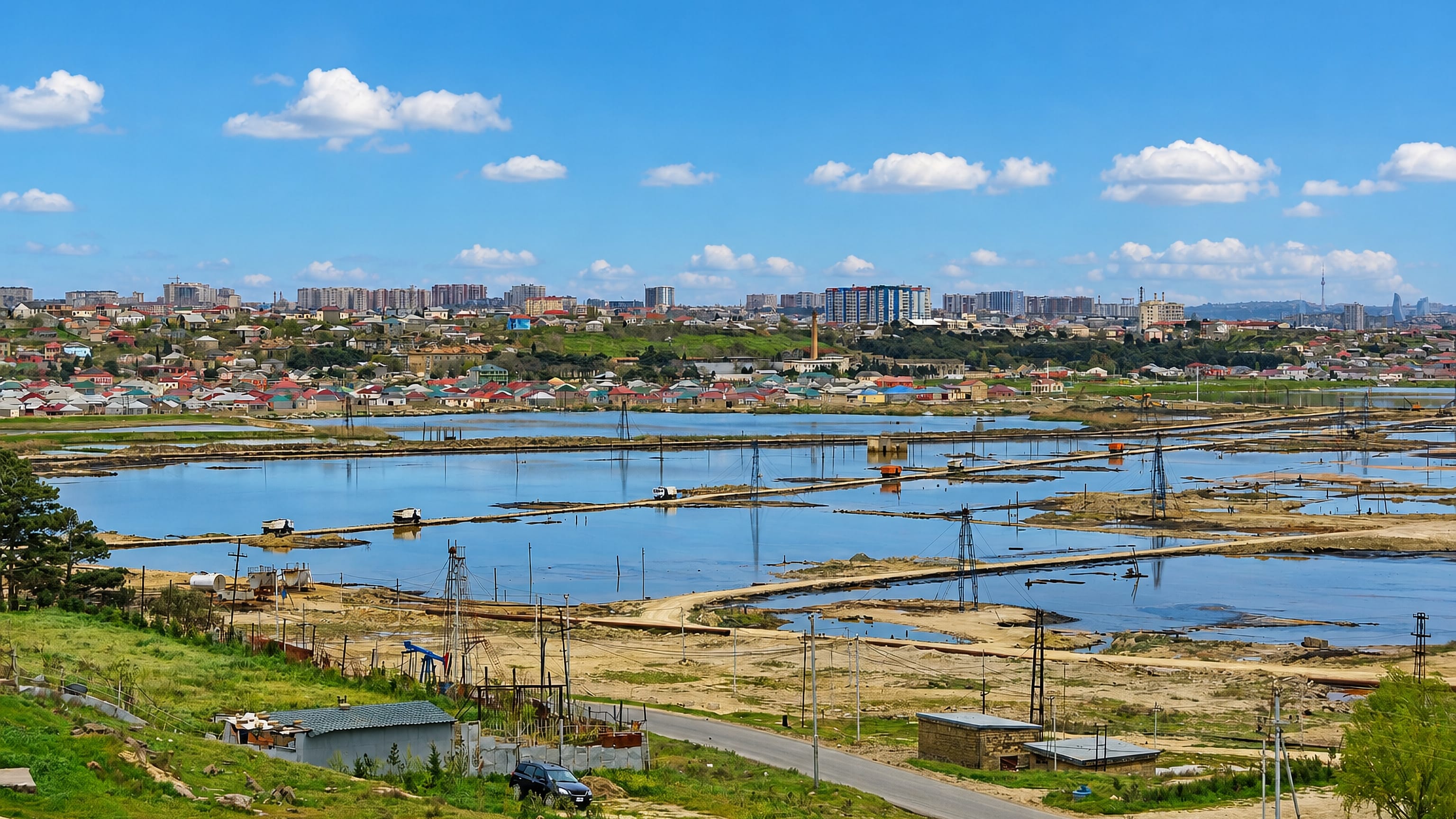 Oil-field flats with pumping derricks fronting a low-rise town and distant Baku skyline at Ramana on the Absheron peninsula