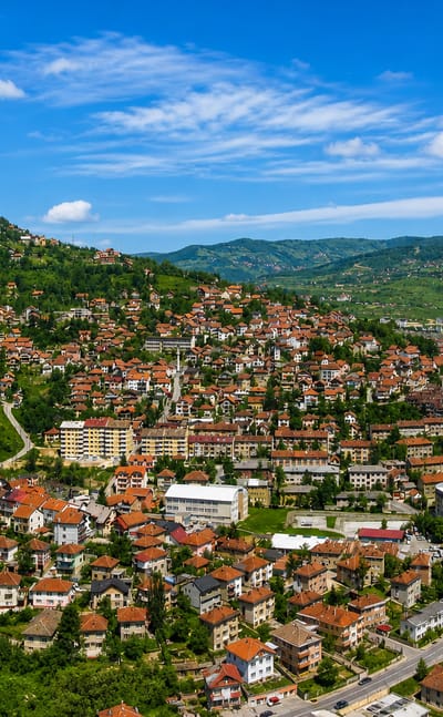 Red-roofed houses climbing the green hills of Sarajevo with the Hum communications tower on the ridge