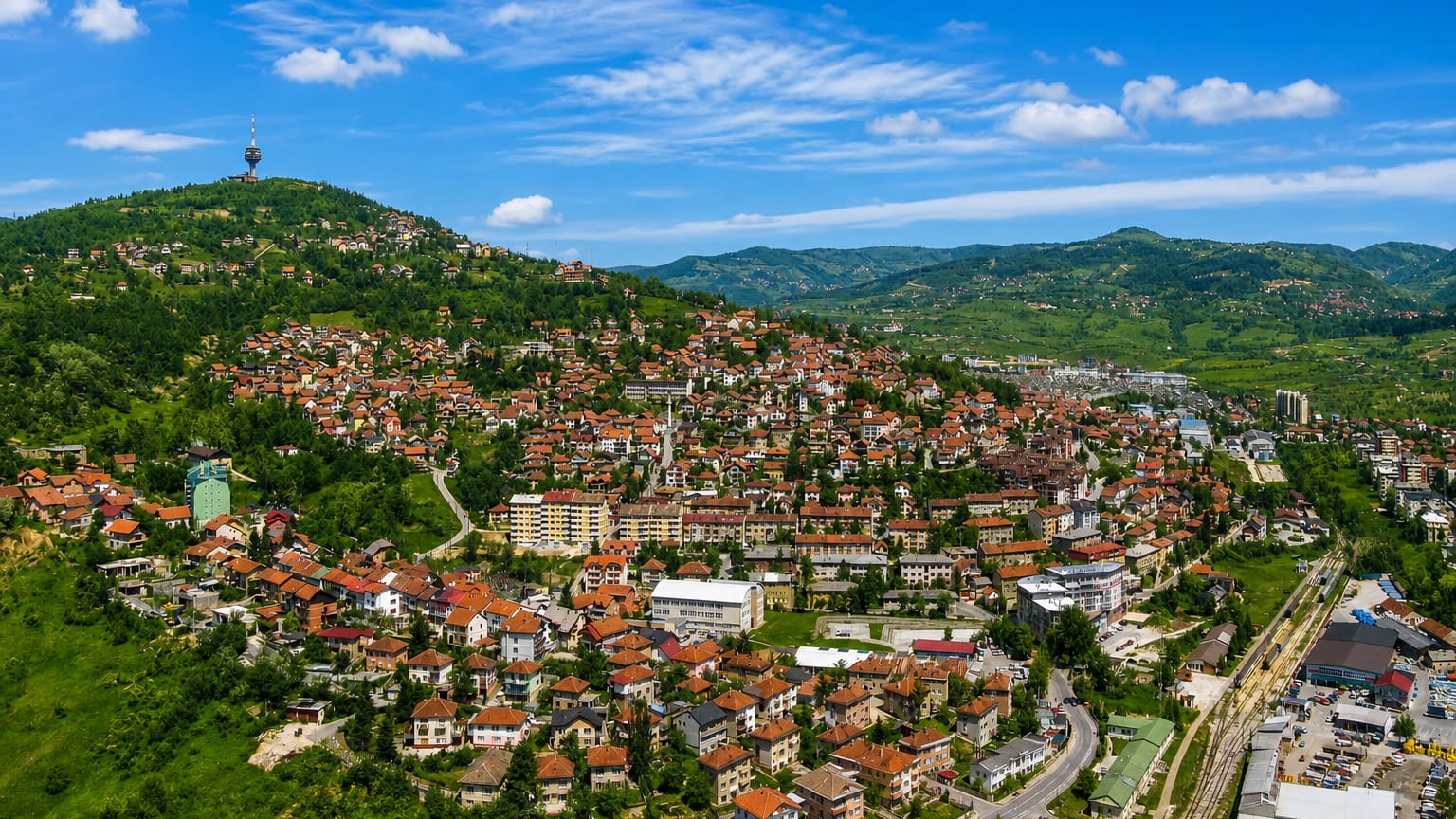 Red-roofed houses climbing the green hills of Sarajevo with the Hum communications tower on the ridge