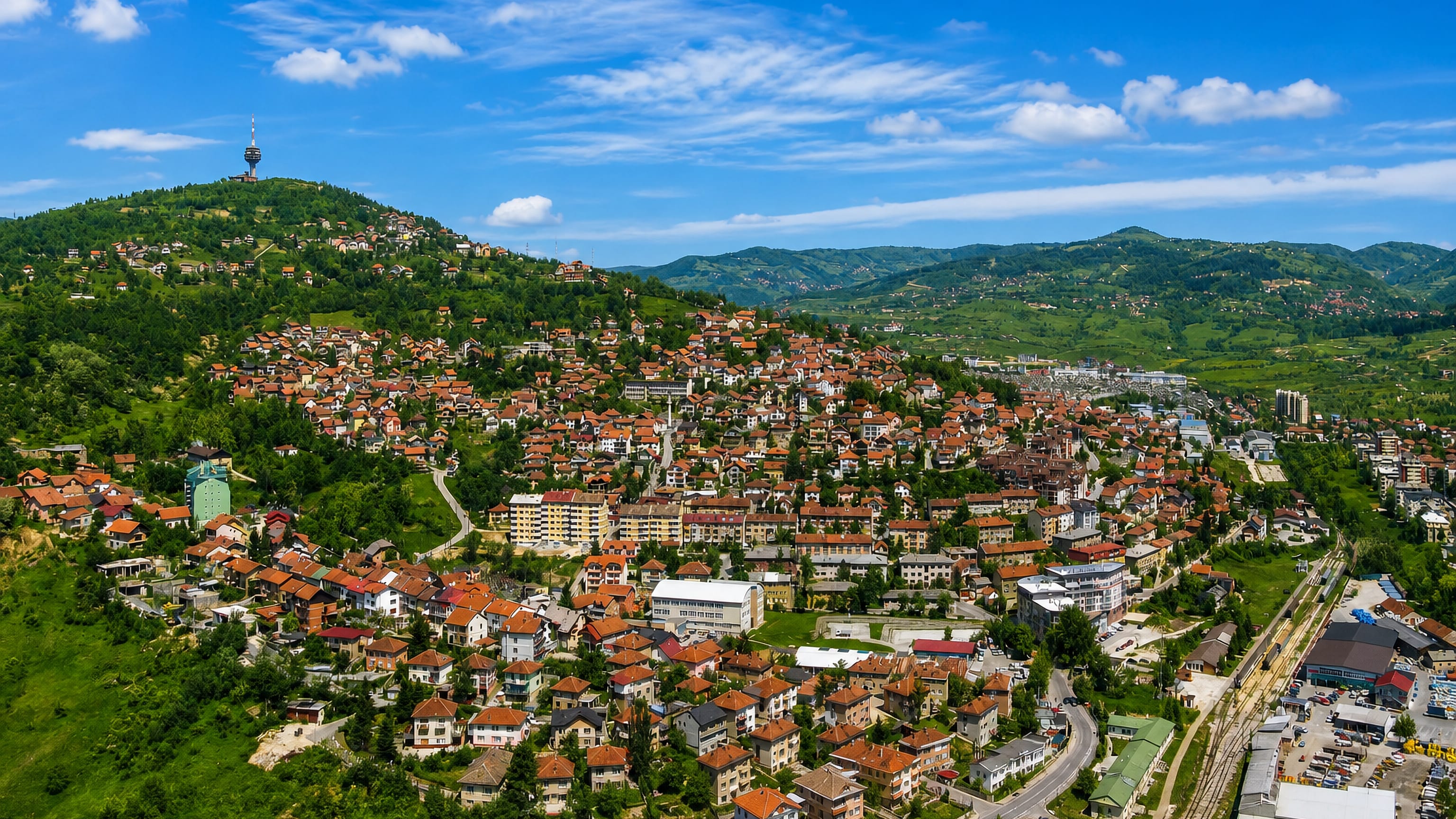 Red-roofed houses climbing the green hills of Sarajevo with the Hum communications tower on the ridge