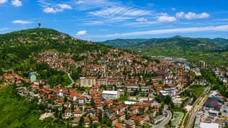 Red-roofed houses climbing the green hills of Sarajevo with the Hum communications tower on the ridge