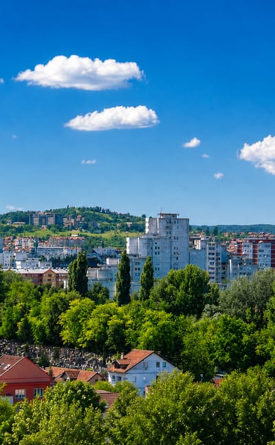 Banja Luka, Bosnia and Herzegovina, with white apartment blocks and red-roofed houses among green trees.
