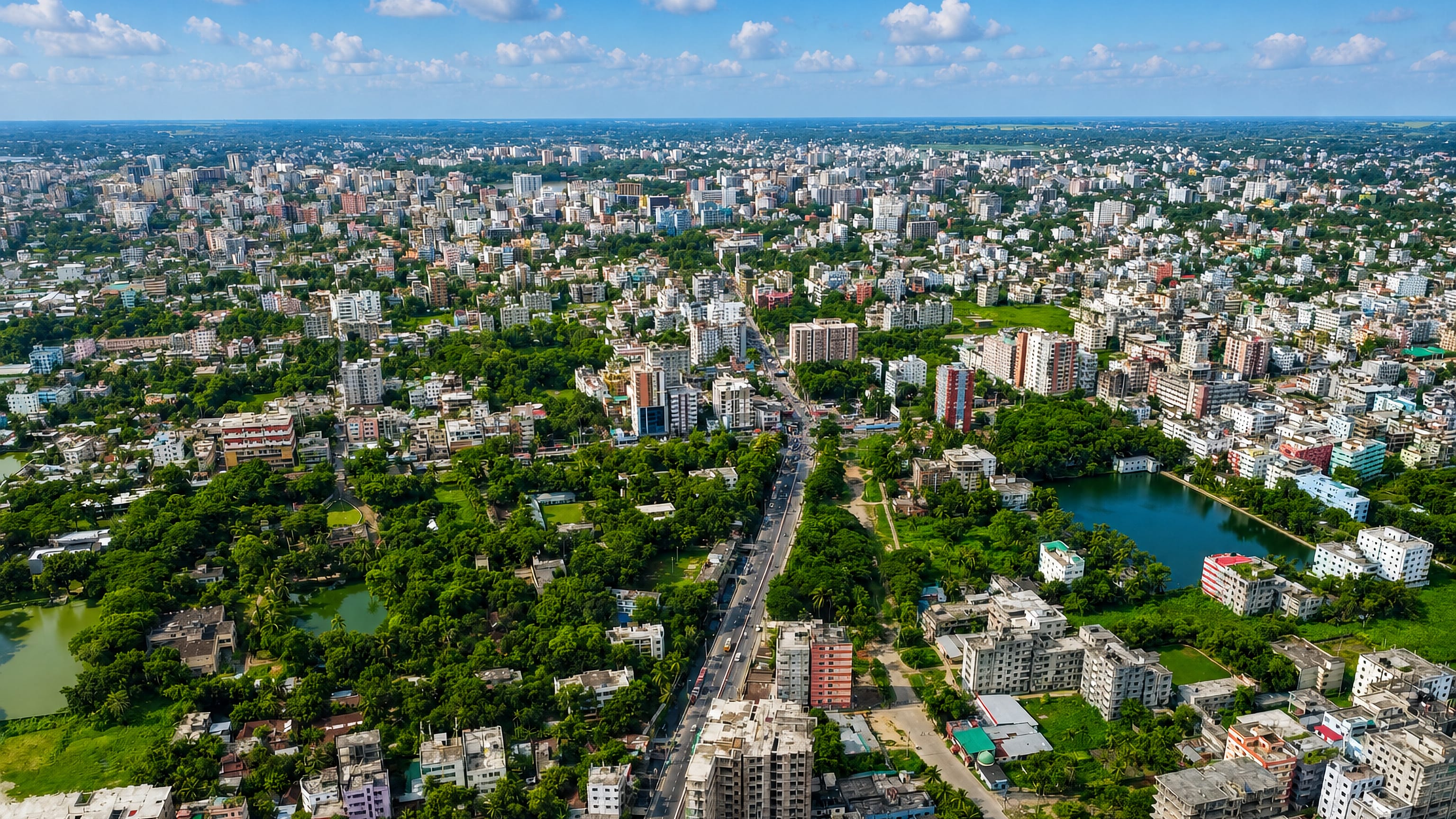 Aerial view over Comilla, Bangladesh, showing dense low-rise blocks, green courtyards, ponds and a main road.