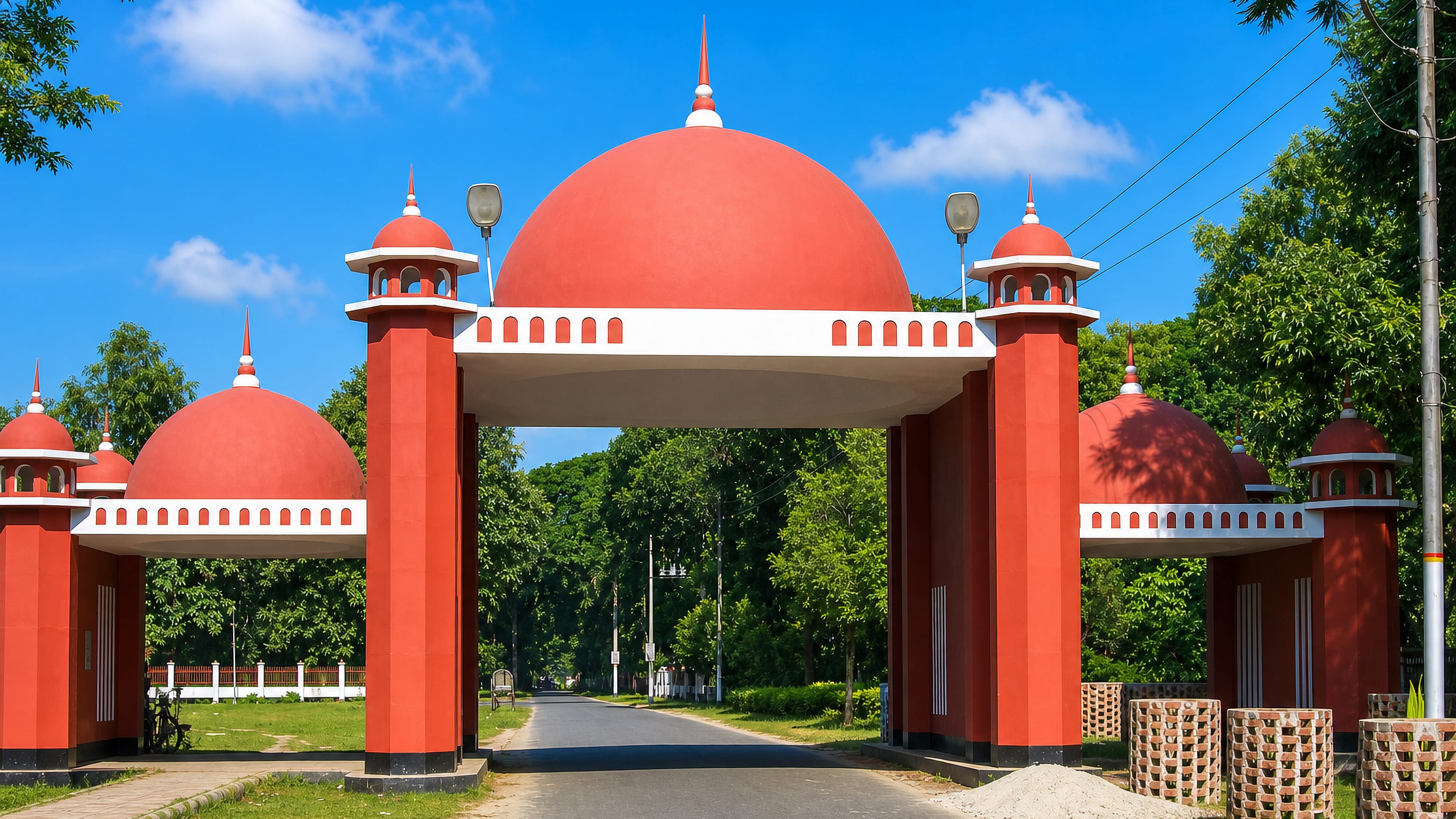 A red-and-white domed ceremonial gateway on a tree-lined road into Tangail, Bangladesh.