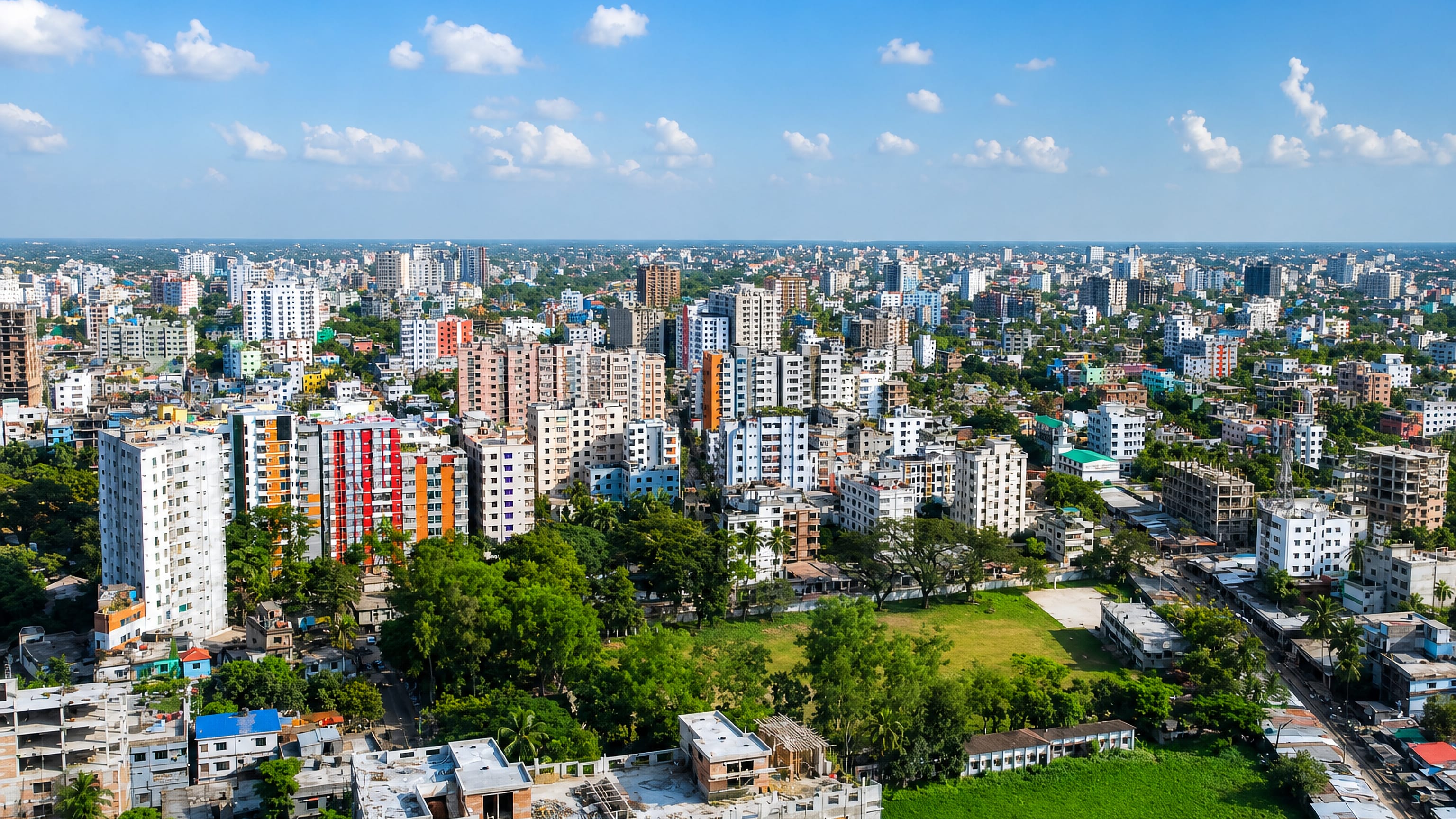 Aerial view of Mymensingh's dense colourful mid-rise blocks and a green playing field, Bangladesh.