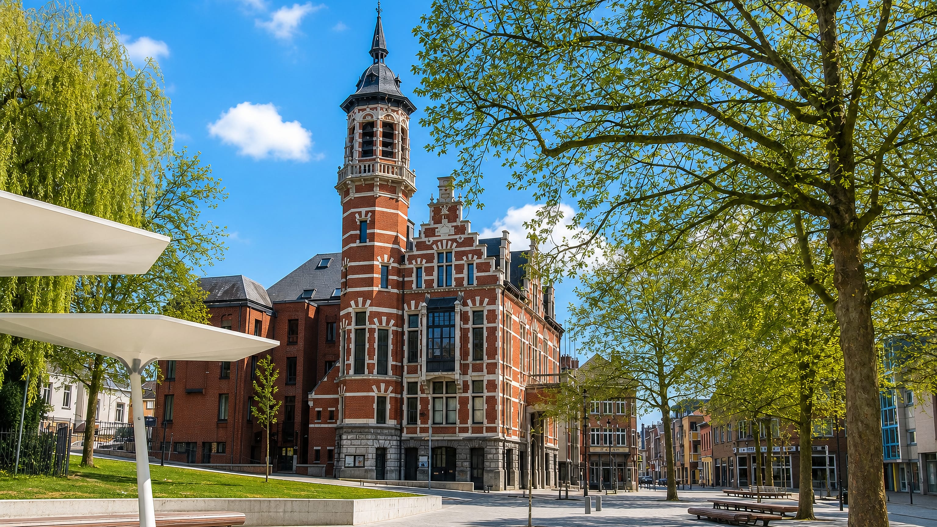 Jette's red-brick neo-Flemish town hall and clock tower rising over a sunlit, tree-lined square in Brussels.