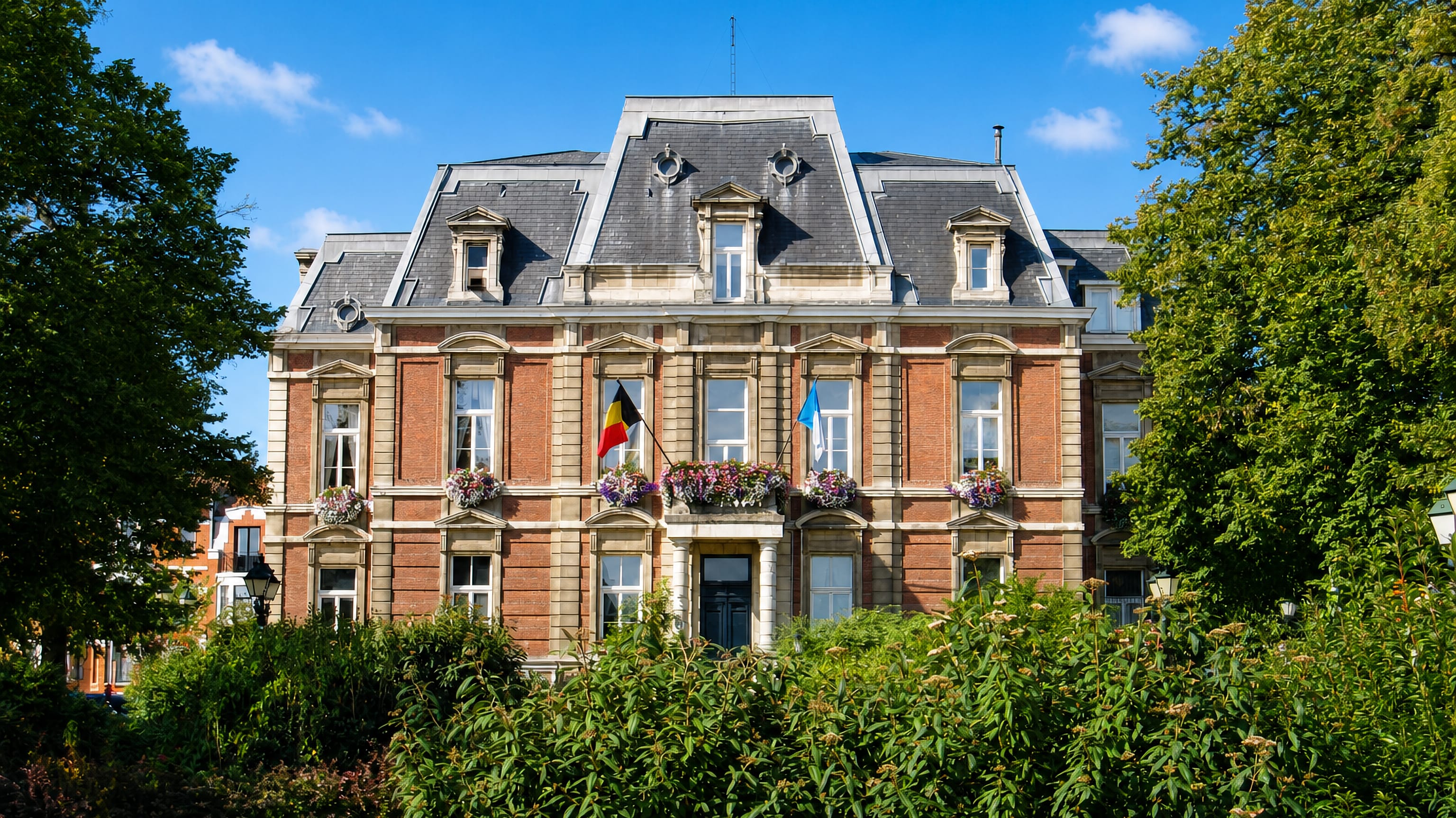 Brick-and-stone communal town hall with Belgian flag and flower boxes in Uccle, Brussels.
