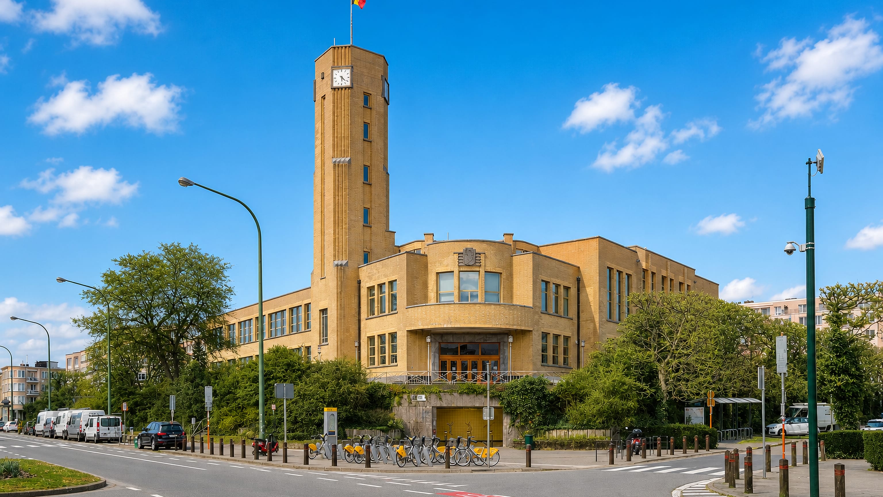 Woluwe-Saint-Lambert's Art Deco town hall and clock tower above a sunlit Brussels boulevard with bike-share racks
