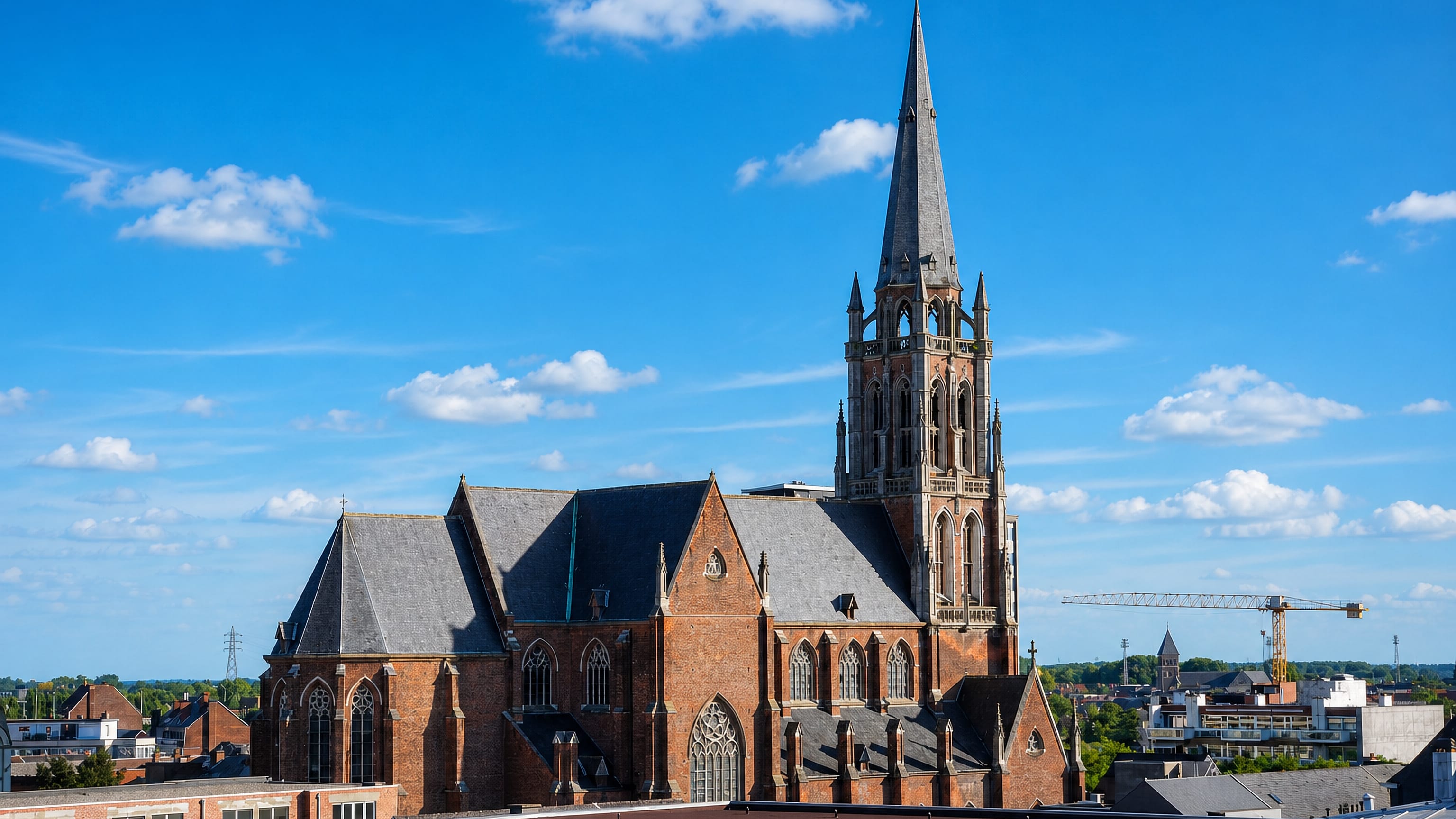 Large brick Gothic church with a tall stone spire rising above rooftops in Aalst, Belgium.