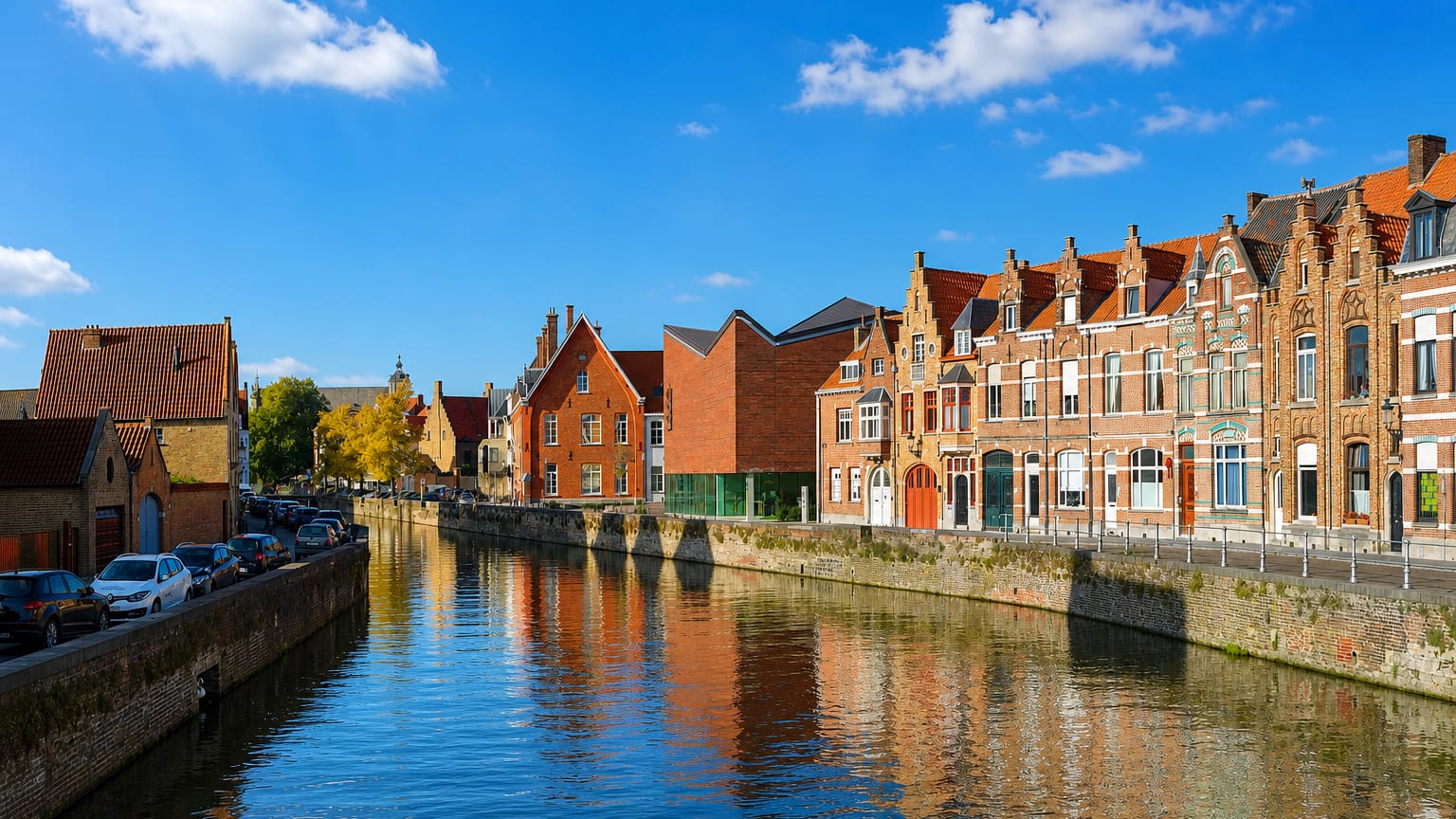 A Bruges canal lined with stepped-gable brick houses reflected in still water under a blue sky.