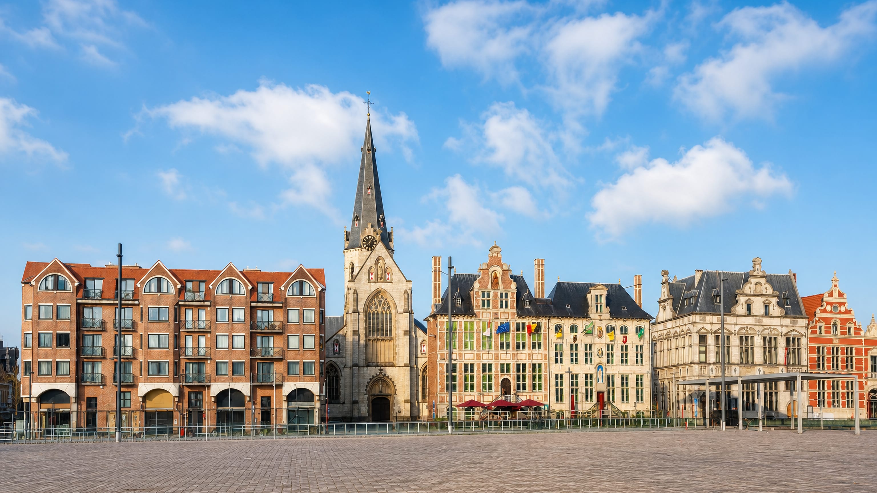 Church spire and stepped-gable houses lining the wide brick market square of Sint-Niklaas, Belgium.