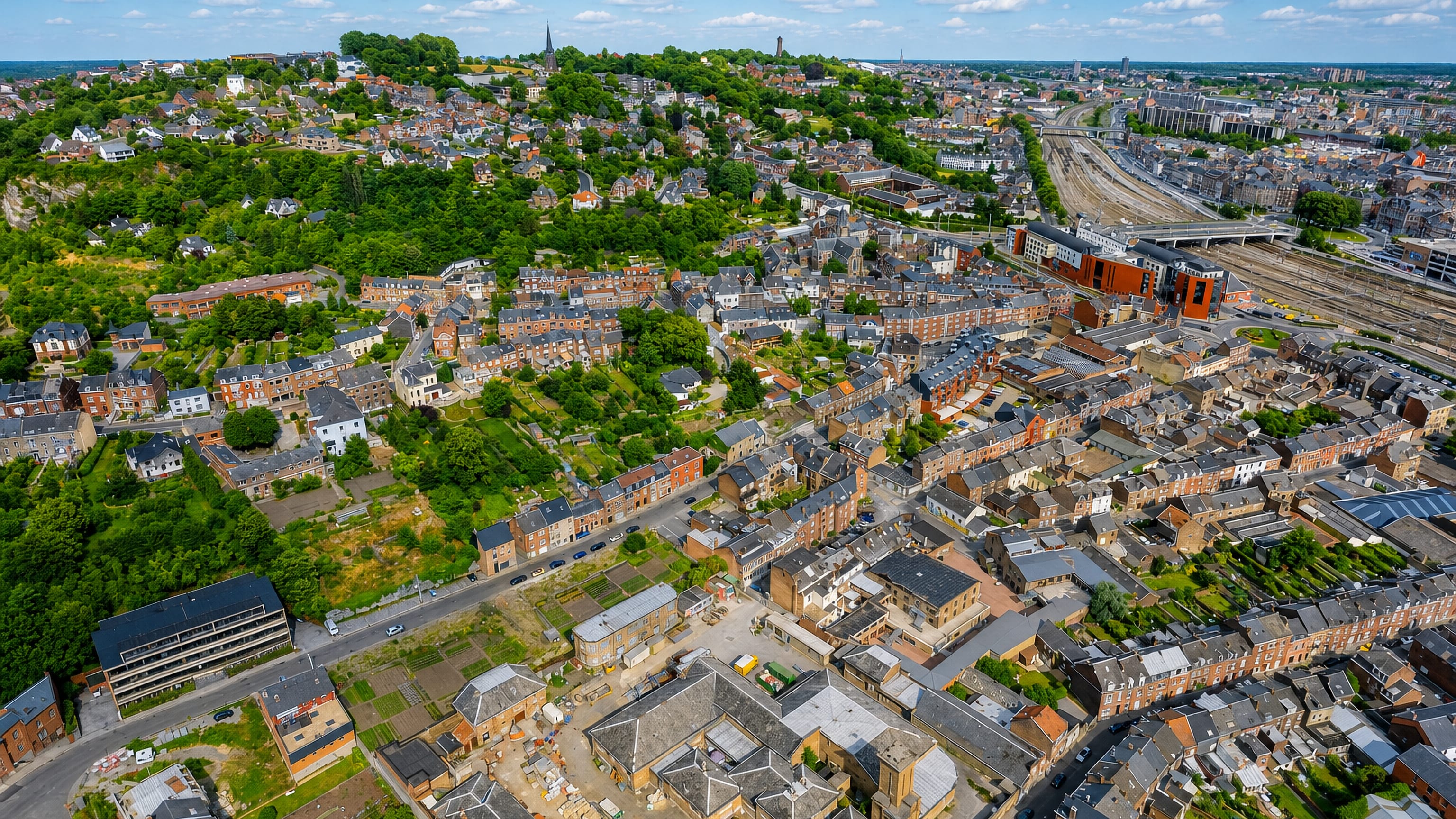 Aerial view over Bomel in Namur, with slate-roofed brick terraces, a church spire and railway yards.