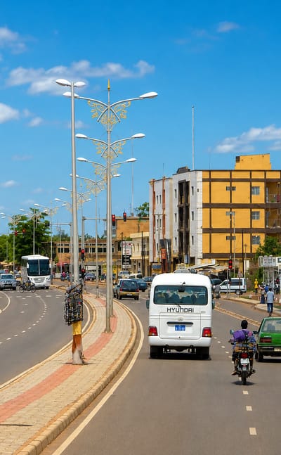 A wide palm-lit boulevard in Ouagadougou, Burkina Faso, busy with motorbikes, minibuses and cars.