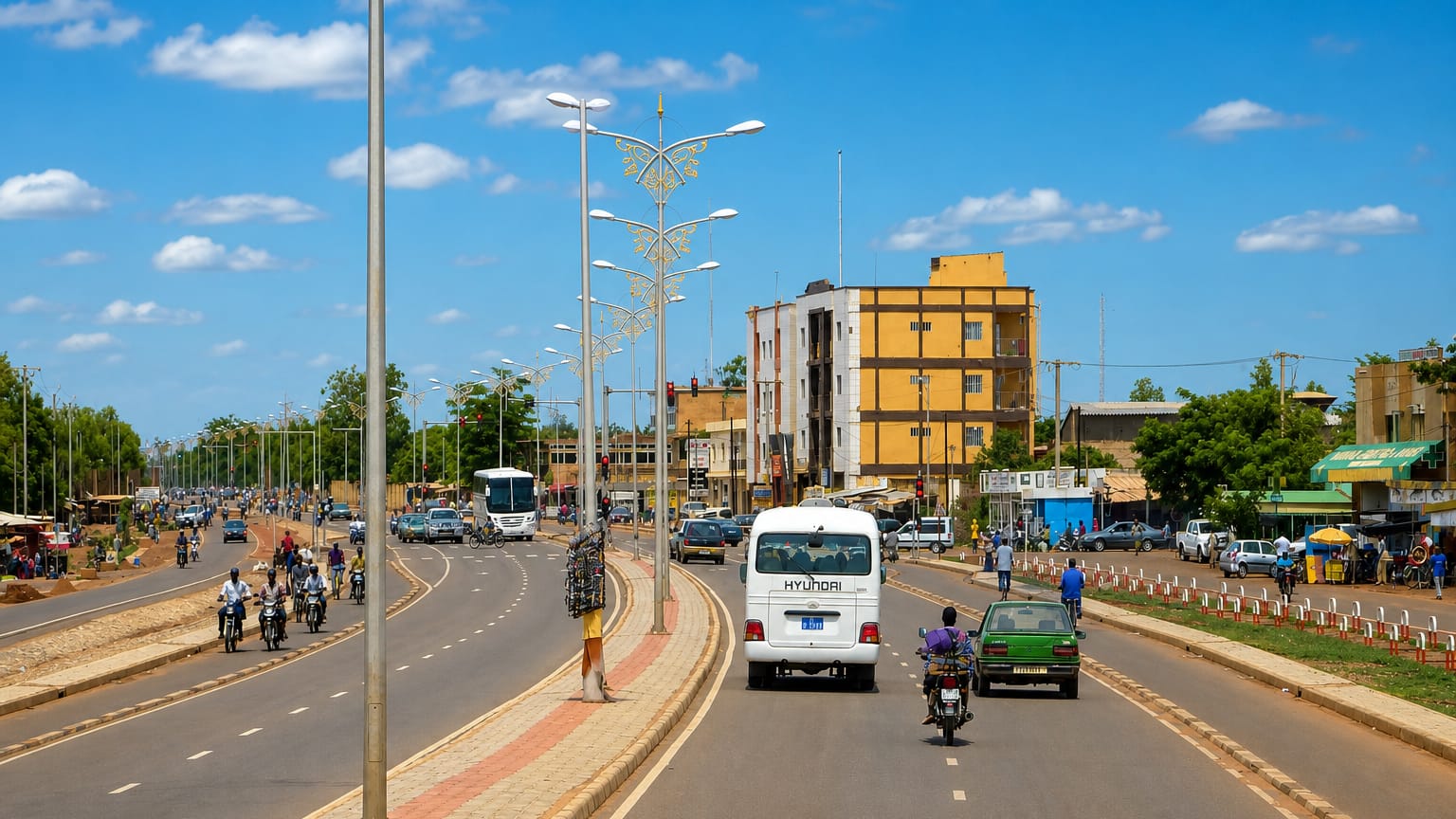 A wide palm-lit boulevard in Ouagadougou, Burkina Faso, busy with motorbikes, minibuses and cars.