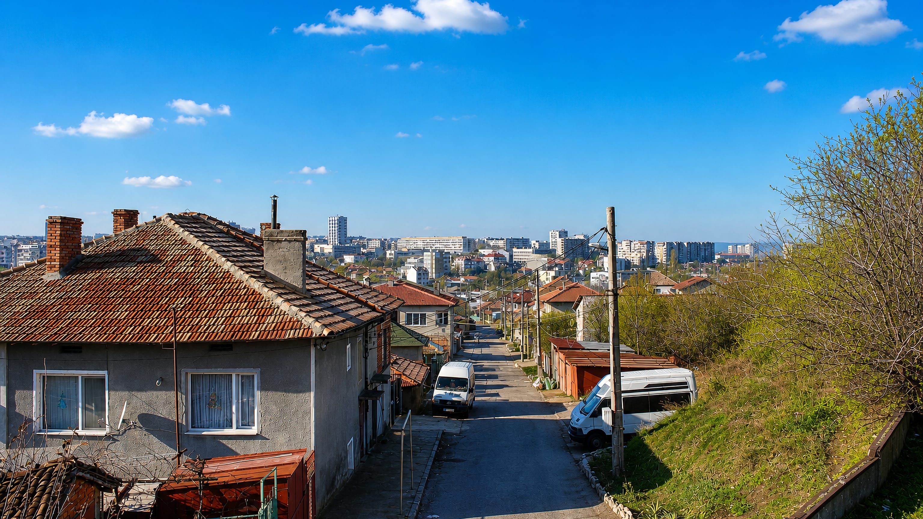 A sloping residential street in Dobrich, Bulgaria, with tiled-roof houses and apartment blocks beyond