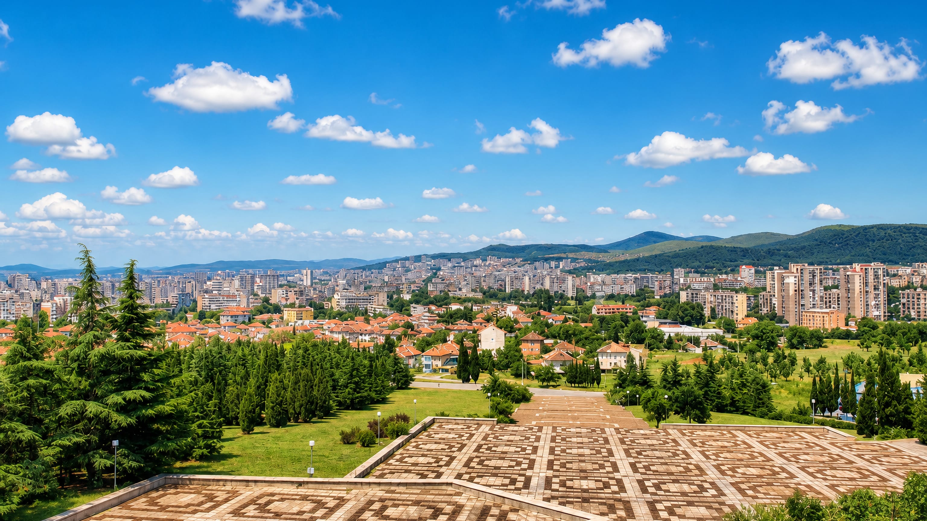 Stara Zagora seen from a paved hilltop terrace, apartment blocks and red roofs below green hills.