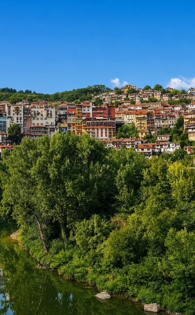 Houses terraced on the hillside above the Yantra River in Veliko Tarnovo, Bulgaria, with the Asenevtsi Monument.