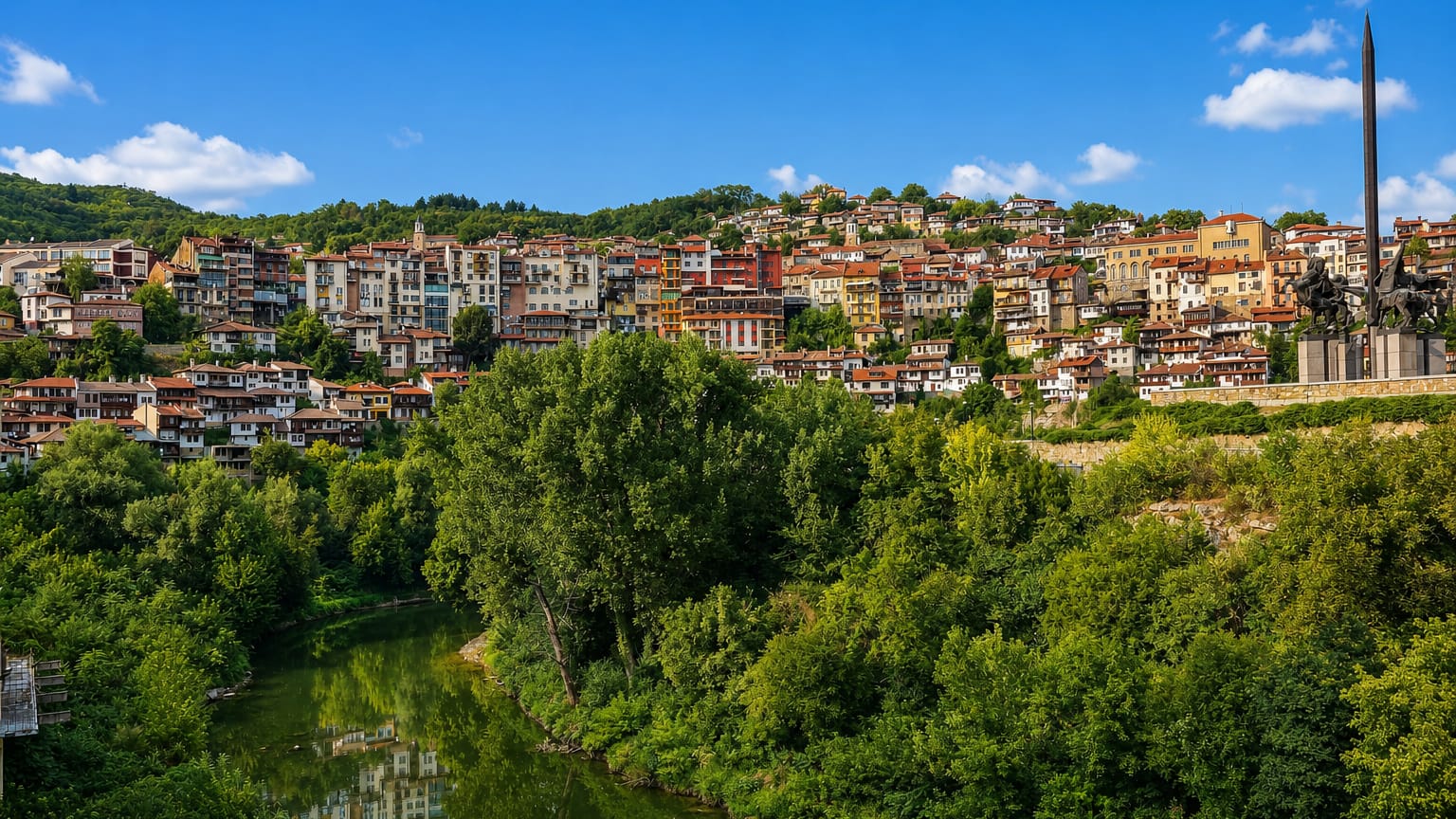 Houses terraced on the hillside above the Yantra River in Veliko Tarnovo, Bulgaria, with the Asenevtsi Monument.