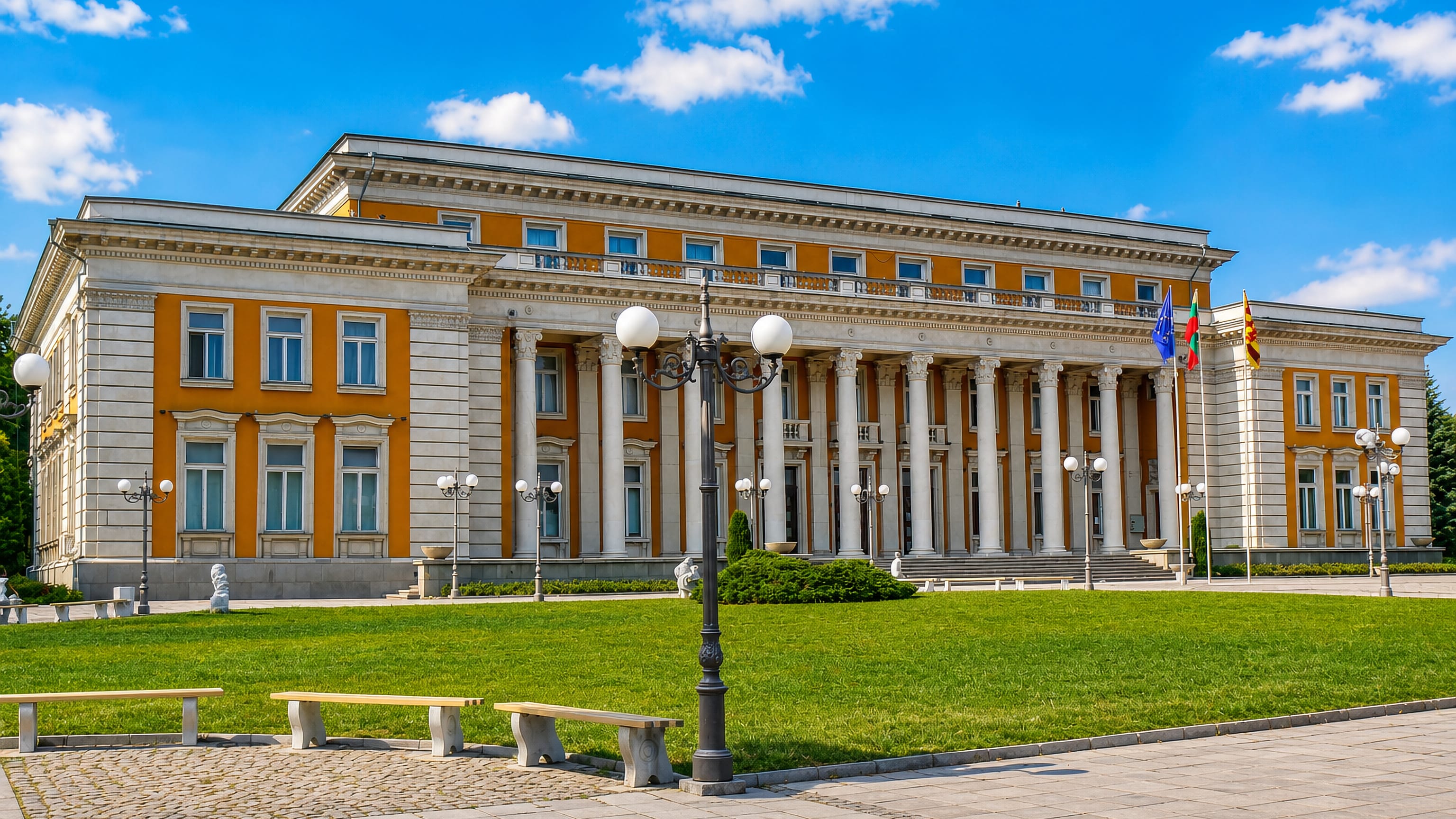 Colonnaded neoclassical culture palace flying Bulgarian flags above lawns and paving in central Pernik.