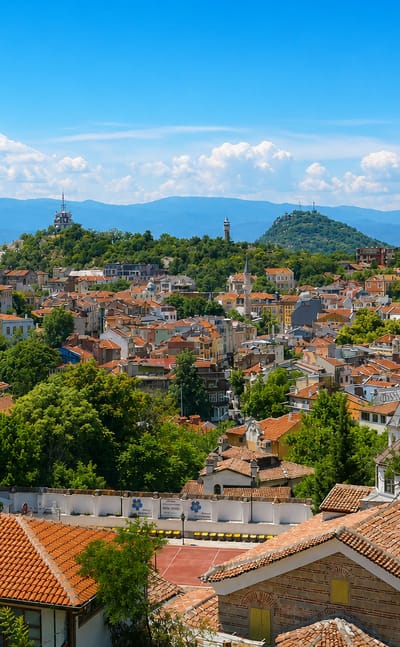Panorama over Plovdiv's red-tiled roofs and wooded hills topped by hilltop monuments.