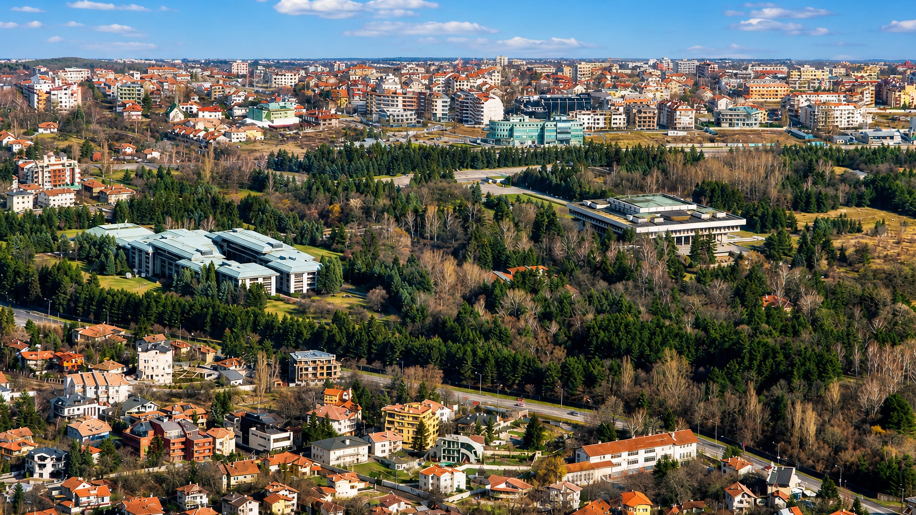 Aerial view over Boyana on Sofia's Vitosha foothills, red-roofed villas and low complexes among pine woods.