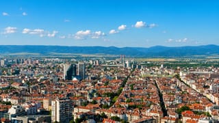 Aerial view of Sofia's dense red-roofed streets stretching toward the Balkan mountains under a clear sky.
