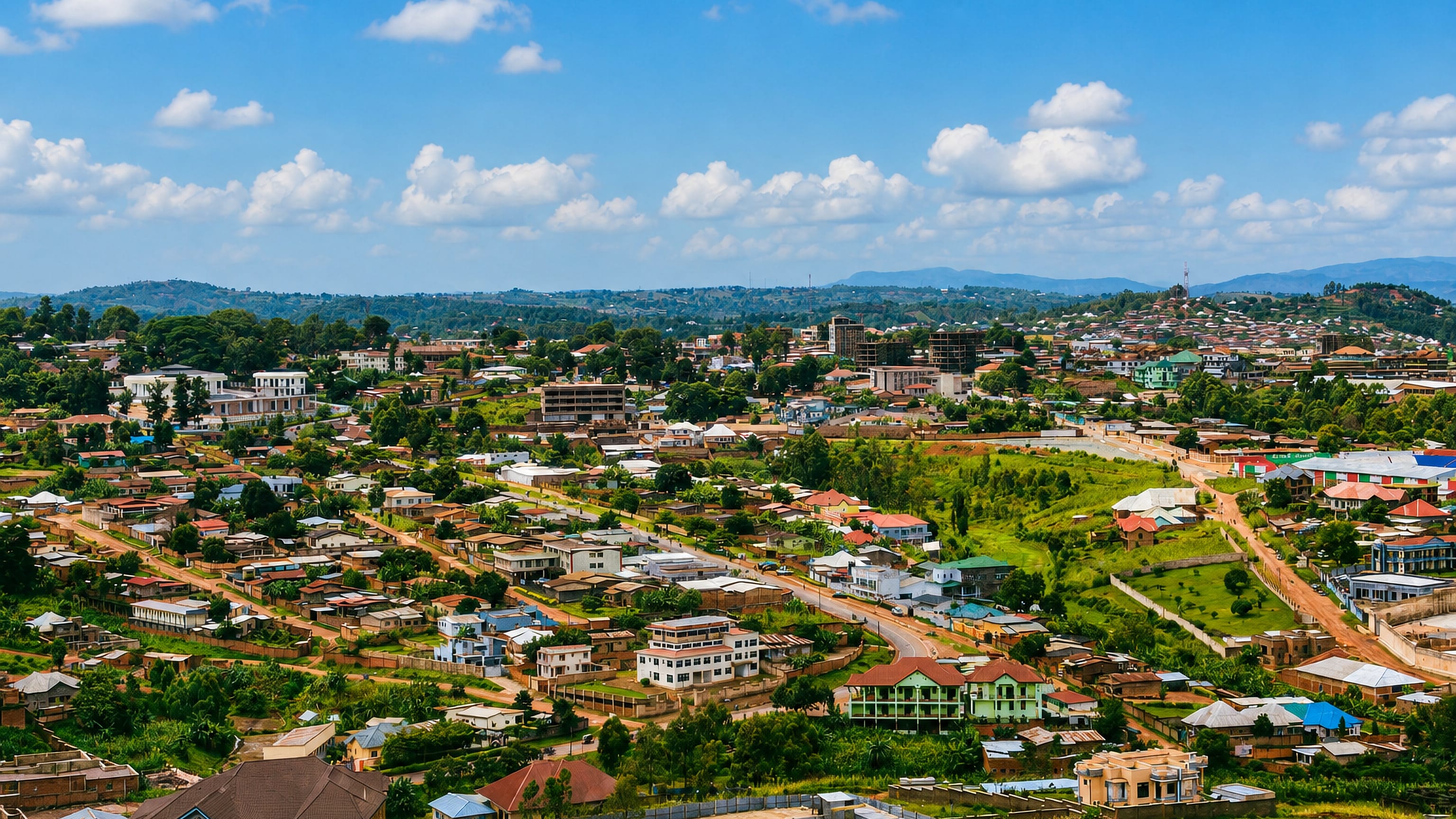 Hillside view over Gitega, Burundi, with tin-roofed houses, red-earth roads and green highland hills beyond