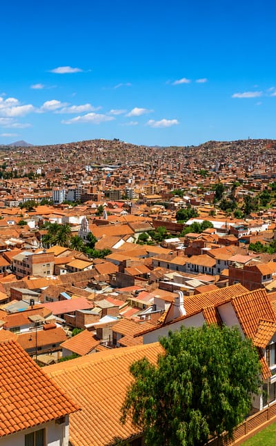 Sucre's terracotta-roofed colonial cityscape across a valley, white church towers rising toward surrounding hills.