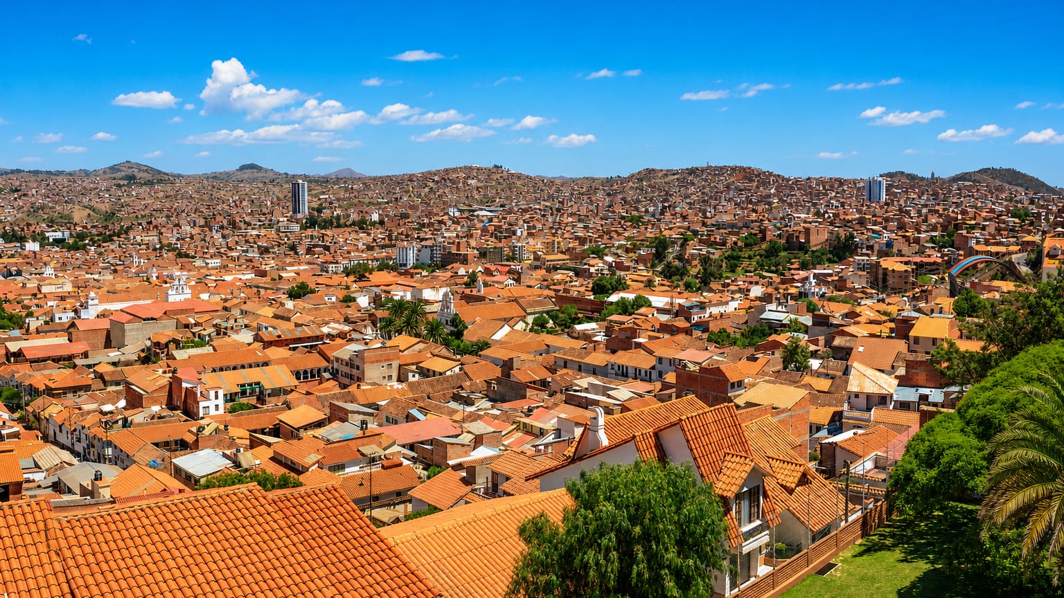 Sucre's terracotta-roofed colonial cityscape across a valley, white church towers rising toward surrounding hills.