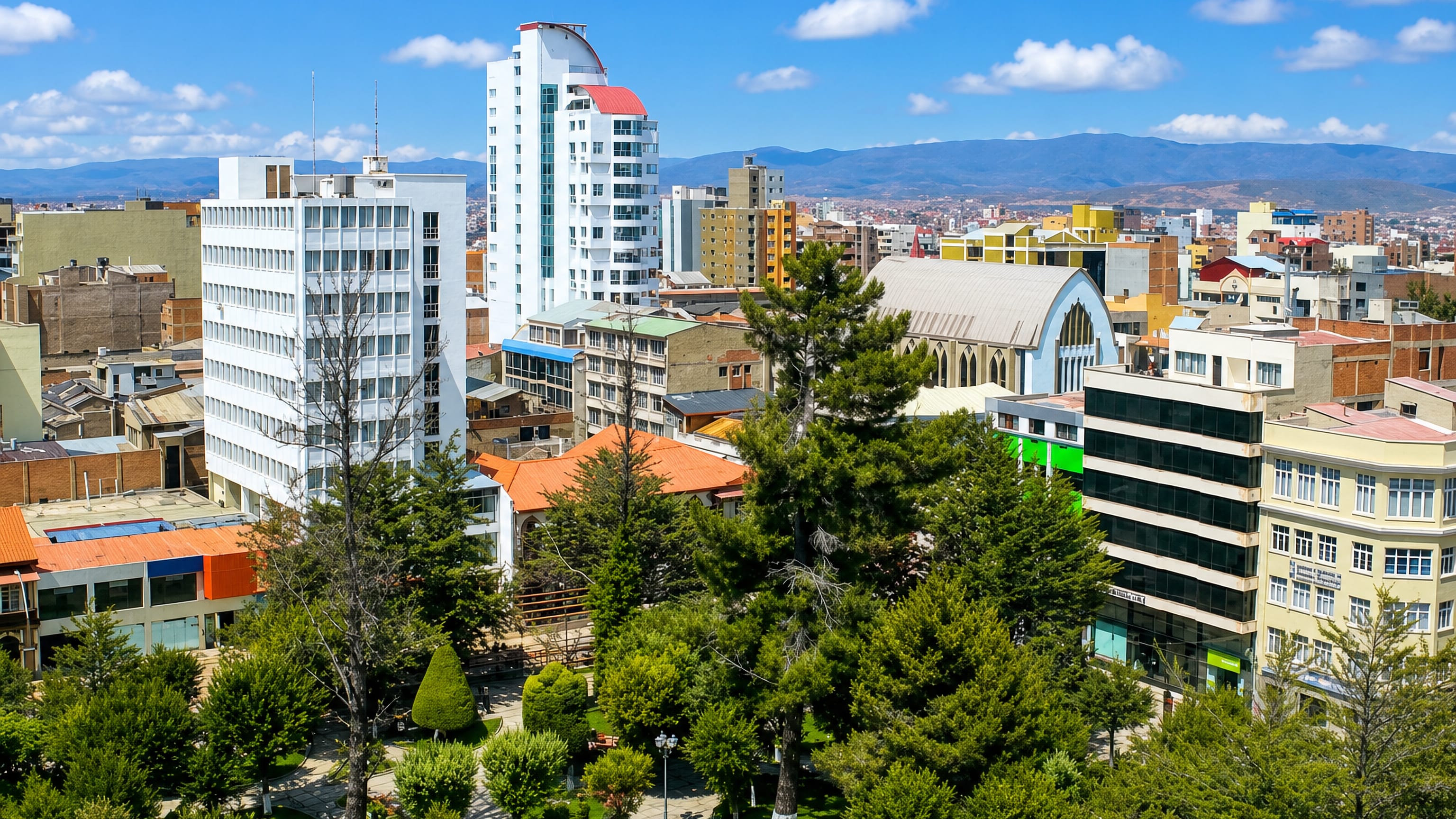 Pine-shaded central plaza in Oruro, Bolivia, ringed by mid-rise blocks with altiplano hills beyond