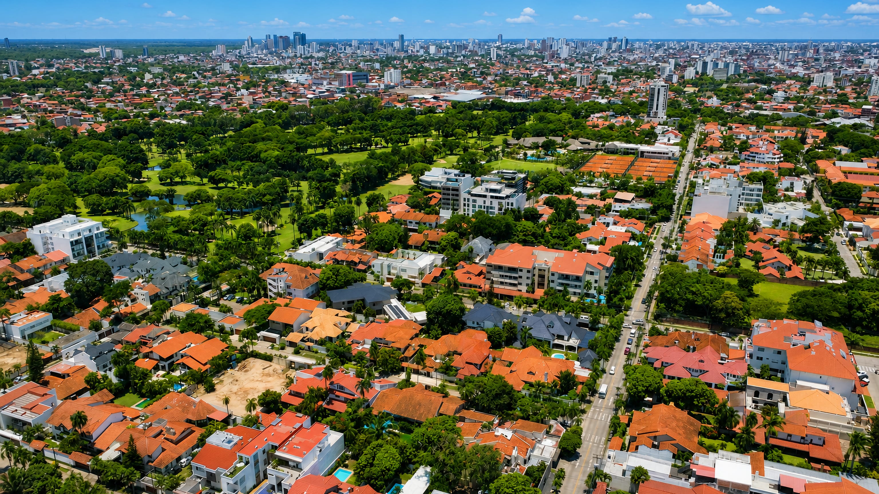Aerial over Las Palmas, a leafy villa district of Santa Cruz de la Sierra, with the city skyline beyond.