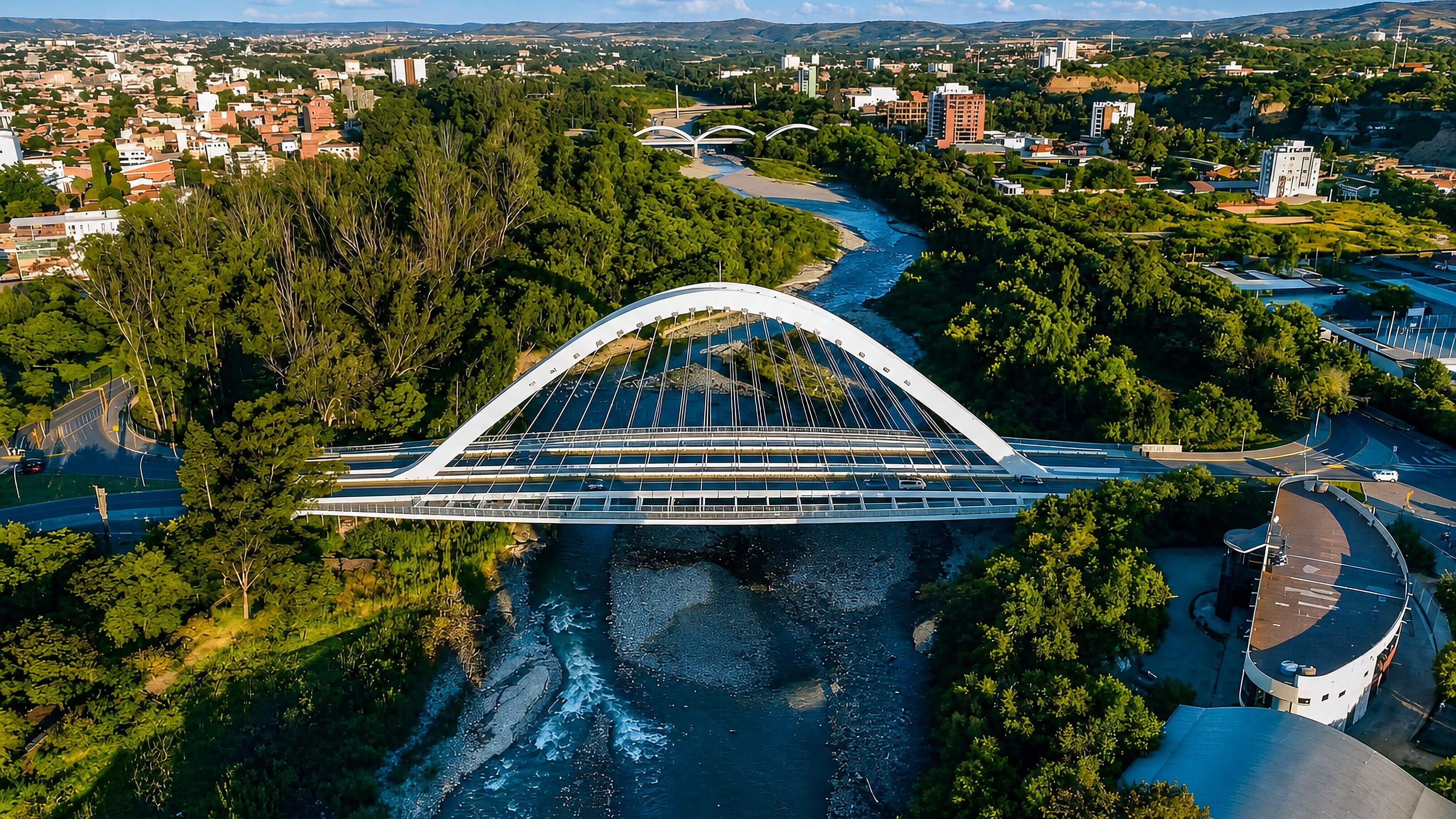 Aerial view of the white arch bridge over the Guadalquivir River in Tarija, Bolivia, with hills beyond.