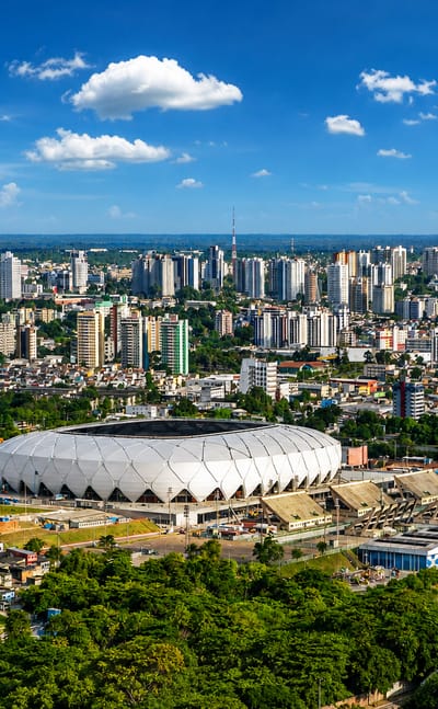 Manaus skyline with the white lattice Arena da Amazonia stadium ringed by Amazon rainforest.