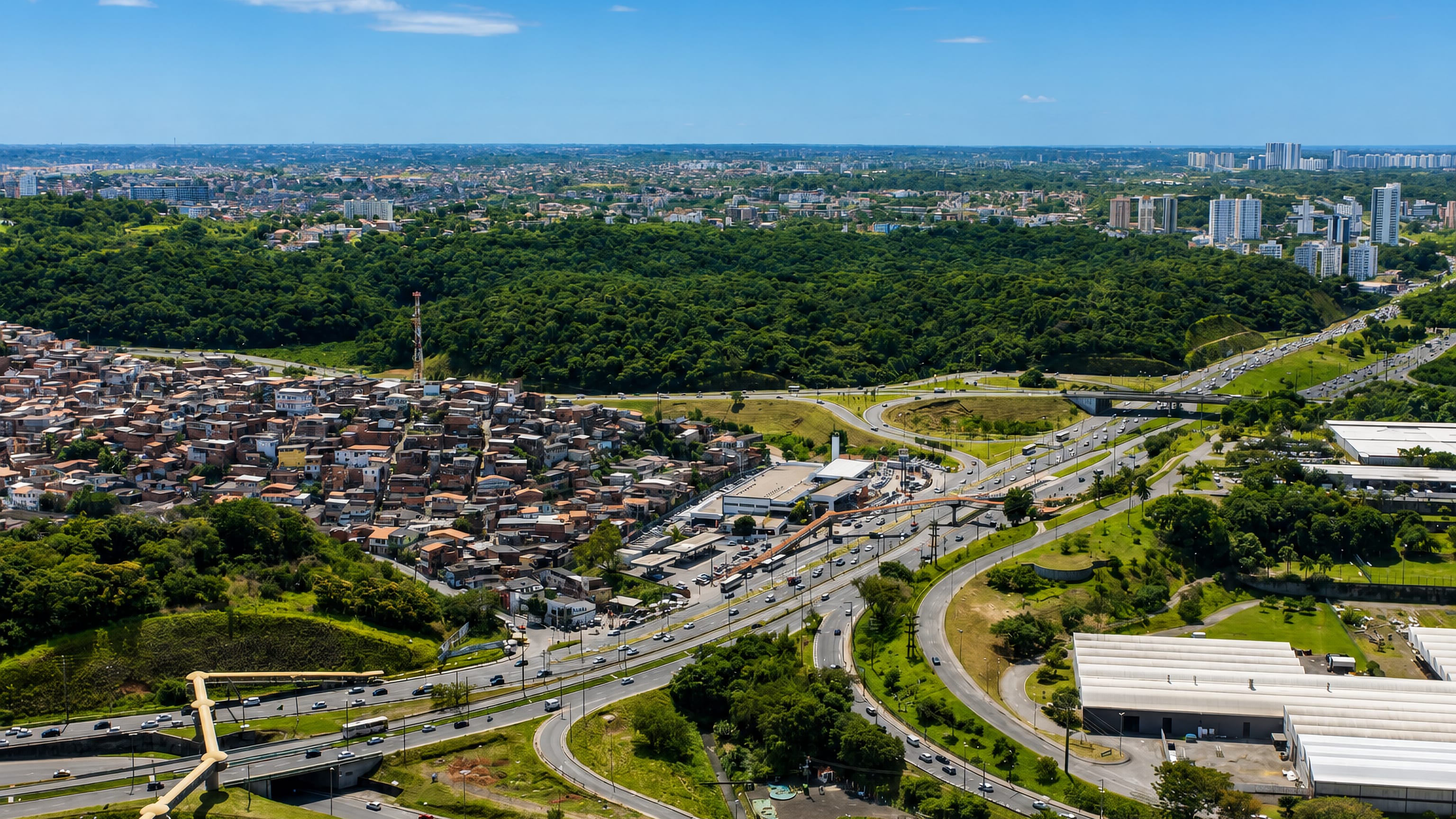 Aerial of Pernambués, Salvador, with dense hillside housing, a highway interchange and green ridges beyond.