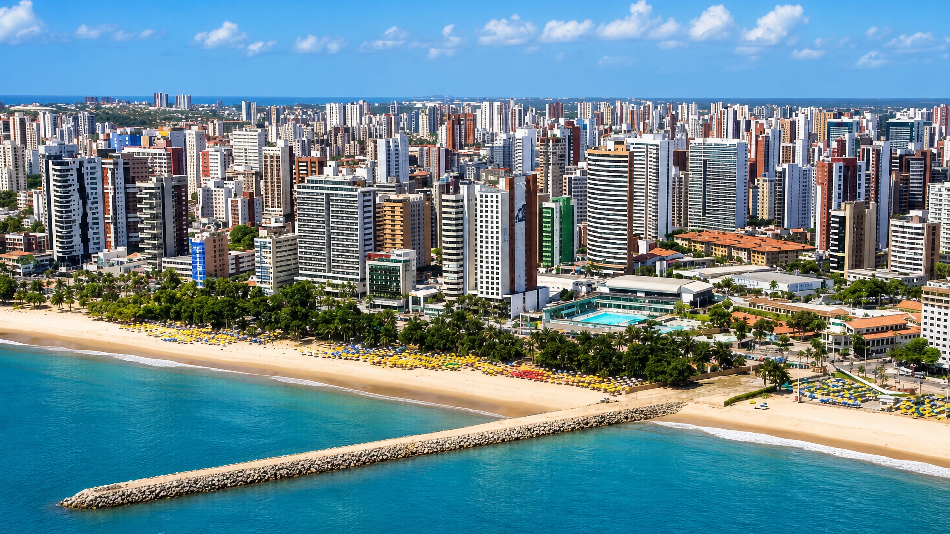 Fortaleza's Beira Mar high-rise skyline above the Atlantic beach, rows of sun umbrellas and a stone breakwater.