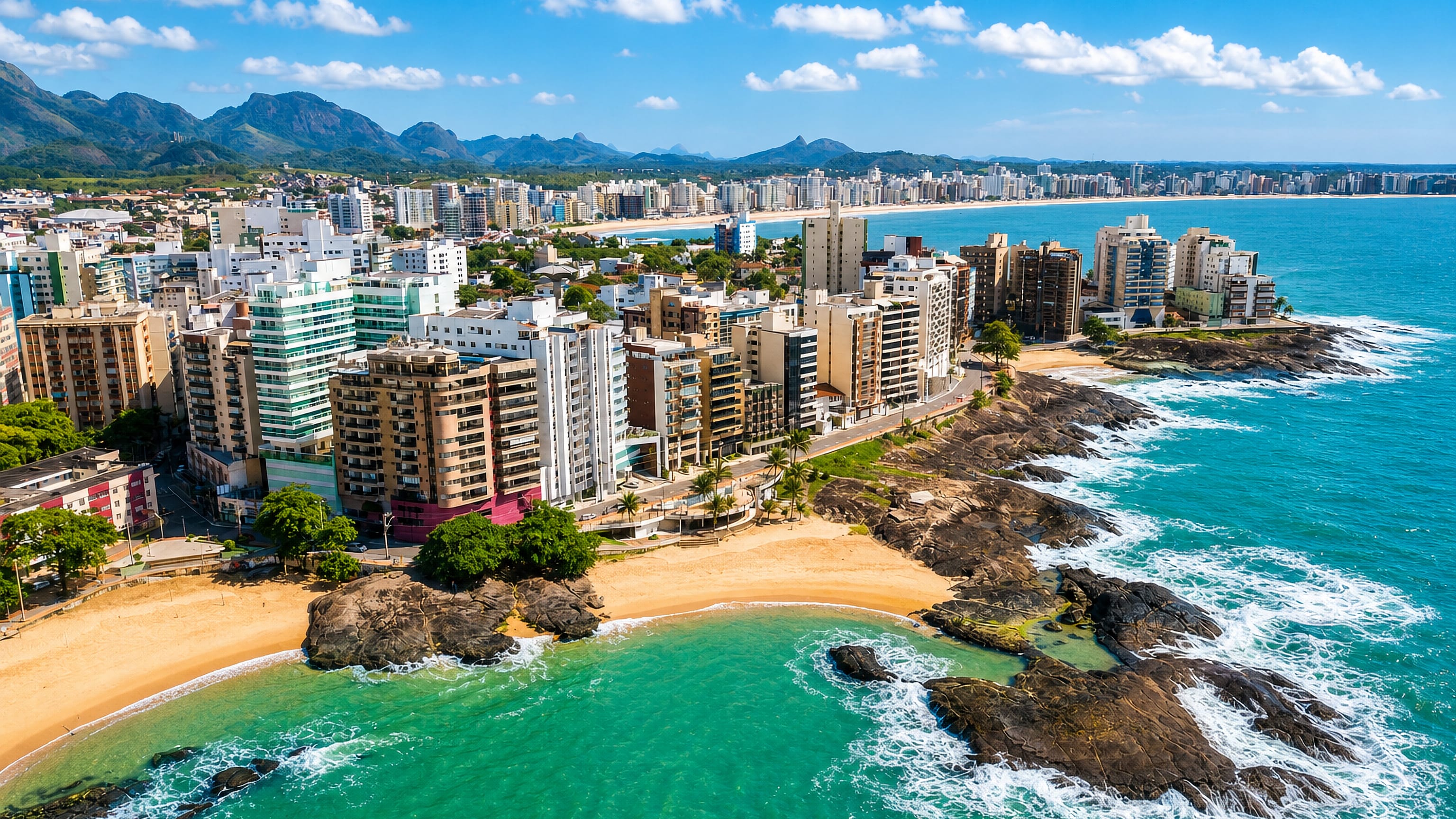 Aerial view of Guarapari, Brazil, with beachfront high-rises, rocky headlands and turquoise coves.