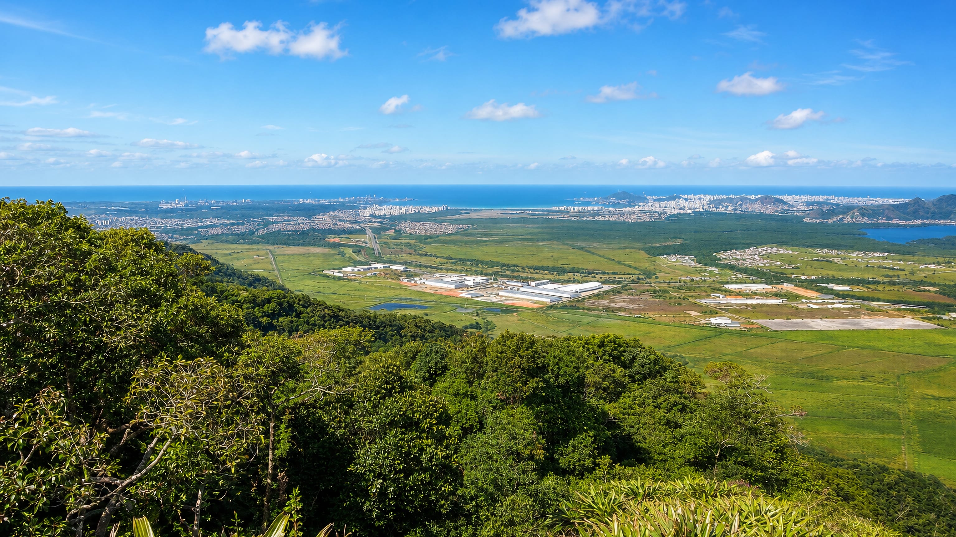 Forested hillside above Serra, Brazil, overlooking warehouses, farmland and the Atlantic coast beyond.