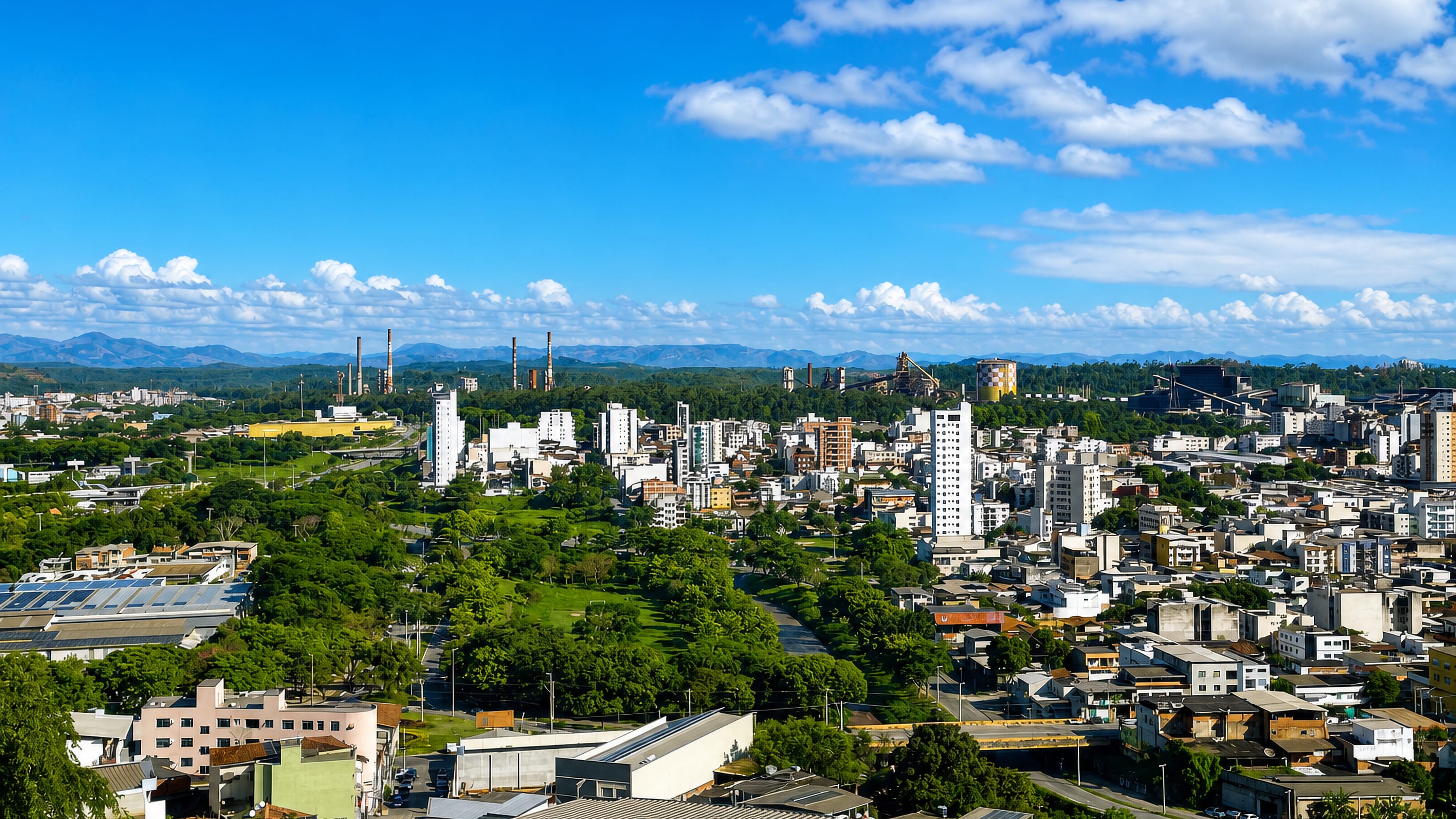 Ipatinga's towers and green avenues below the Usiminas steelworks chimneys and the Vale do Aço mountains.