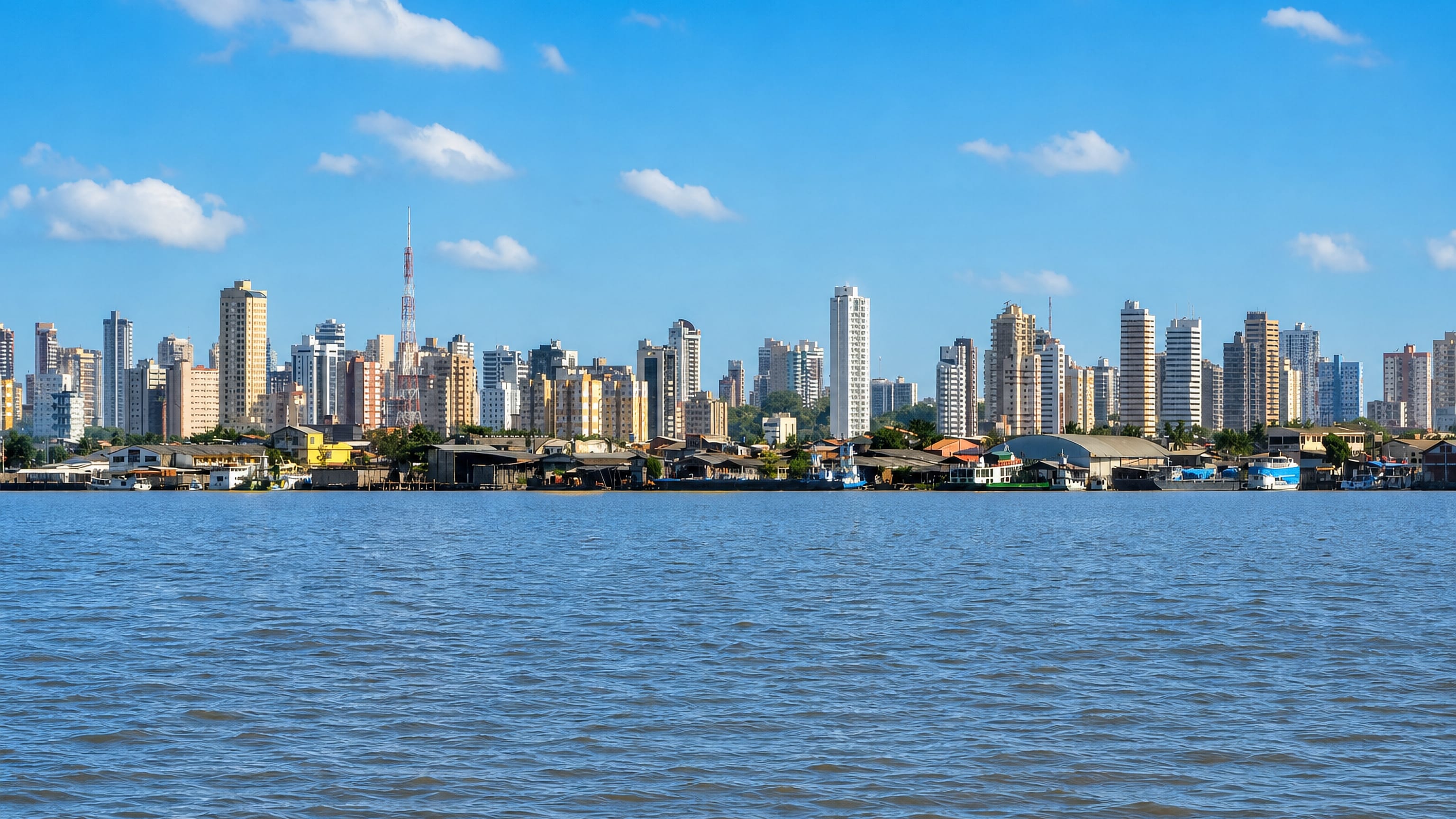 Belem's Guama waterfront seen across the river, with riverside houses backed by a wall of high-rises.