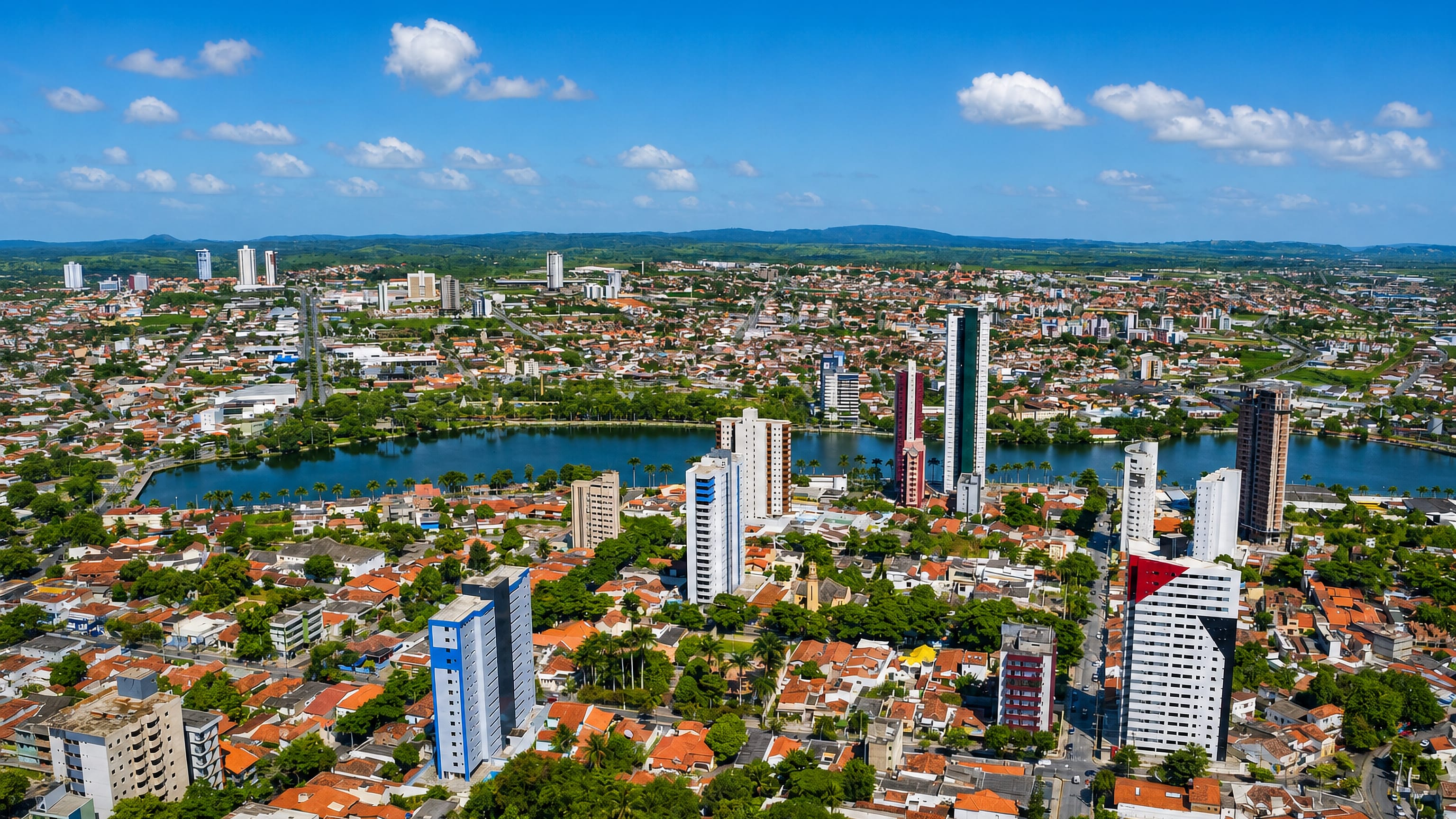 Aerial view of Campina Grande, Brazil, with the palm-lined Açude Velho lake ringed by towers and red-roofed houses.