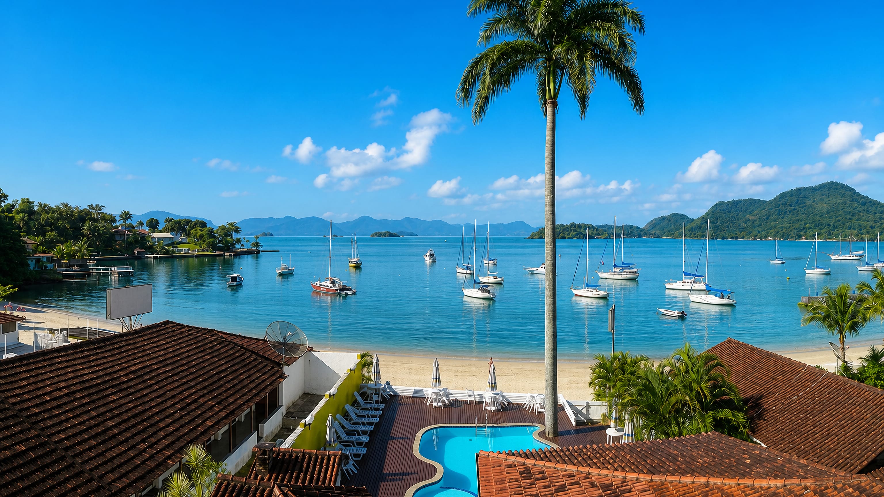 Sailboats moored in the island-dotted bay at Angra dos Reis, Brazil, seen over tiled roofs and a pool terrace.